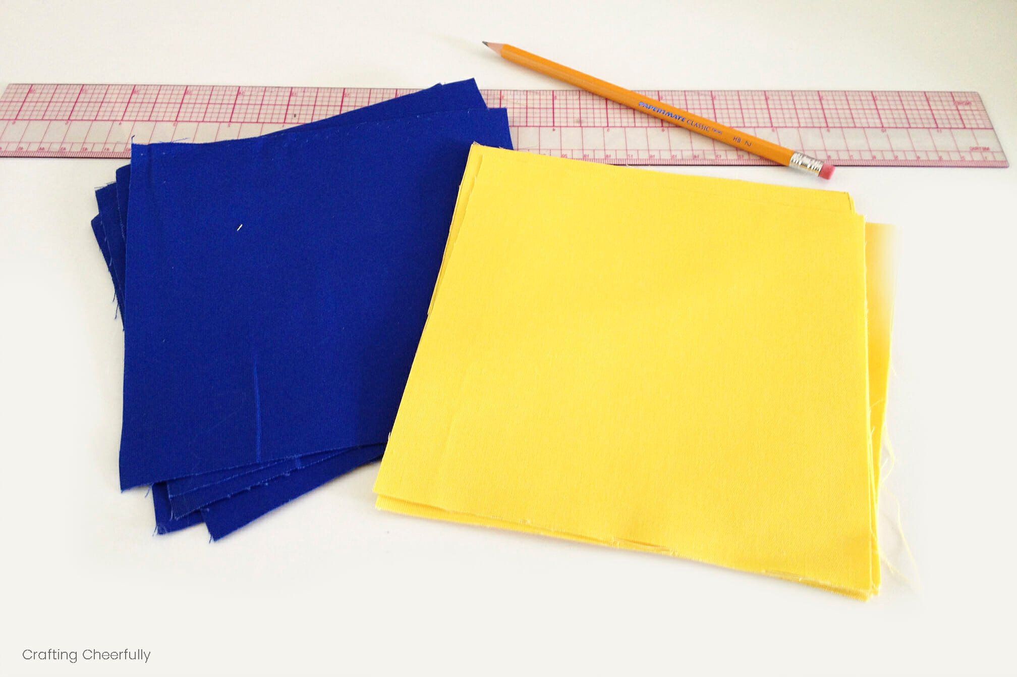 Squares of blue and yellow canvas fabric lay next to a ruler and pencil.