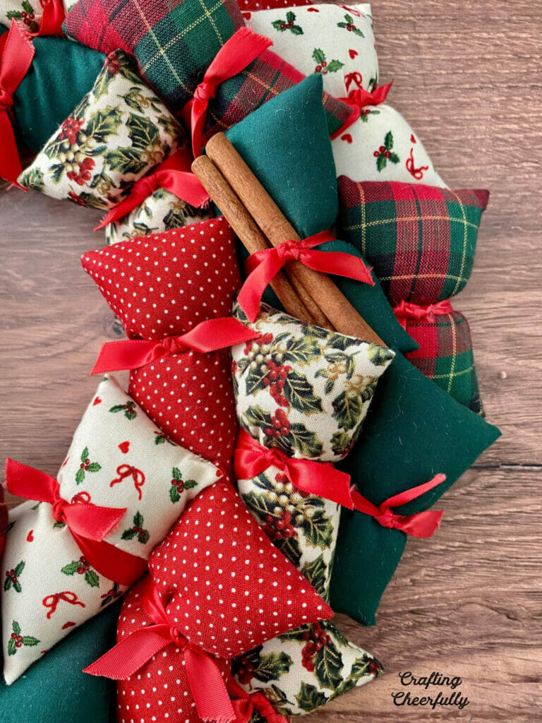 DIY holiday pillow wreath using Christmas fabrics in red, green and white lays on a wooden table.