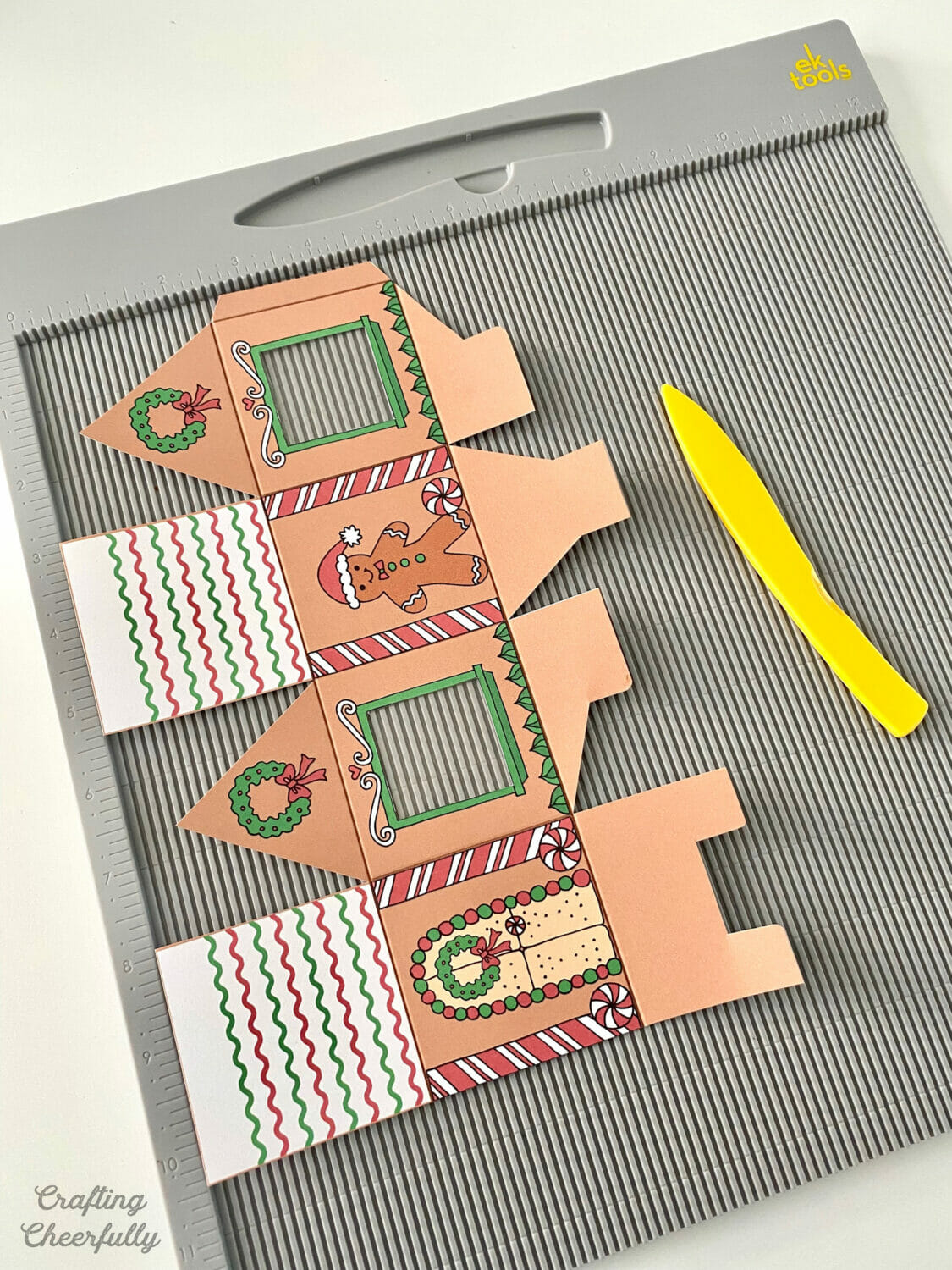 A printable gingerbread treat box is on a scoring board next to a yellow scoring stylus.