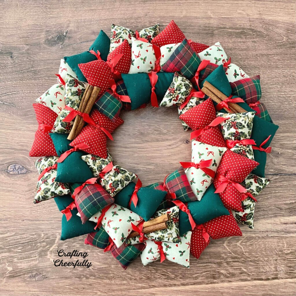 DIY holiday pillow wreath using Christmas fabrics in red, green and white lays on a wooden table.