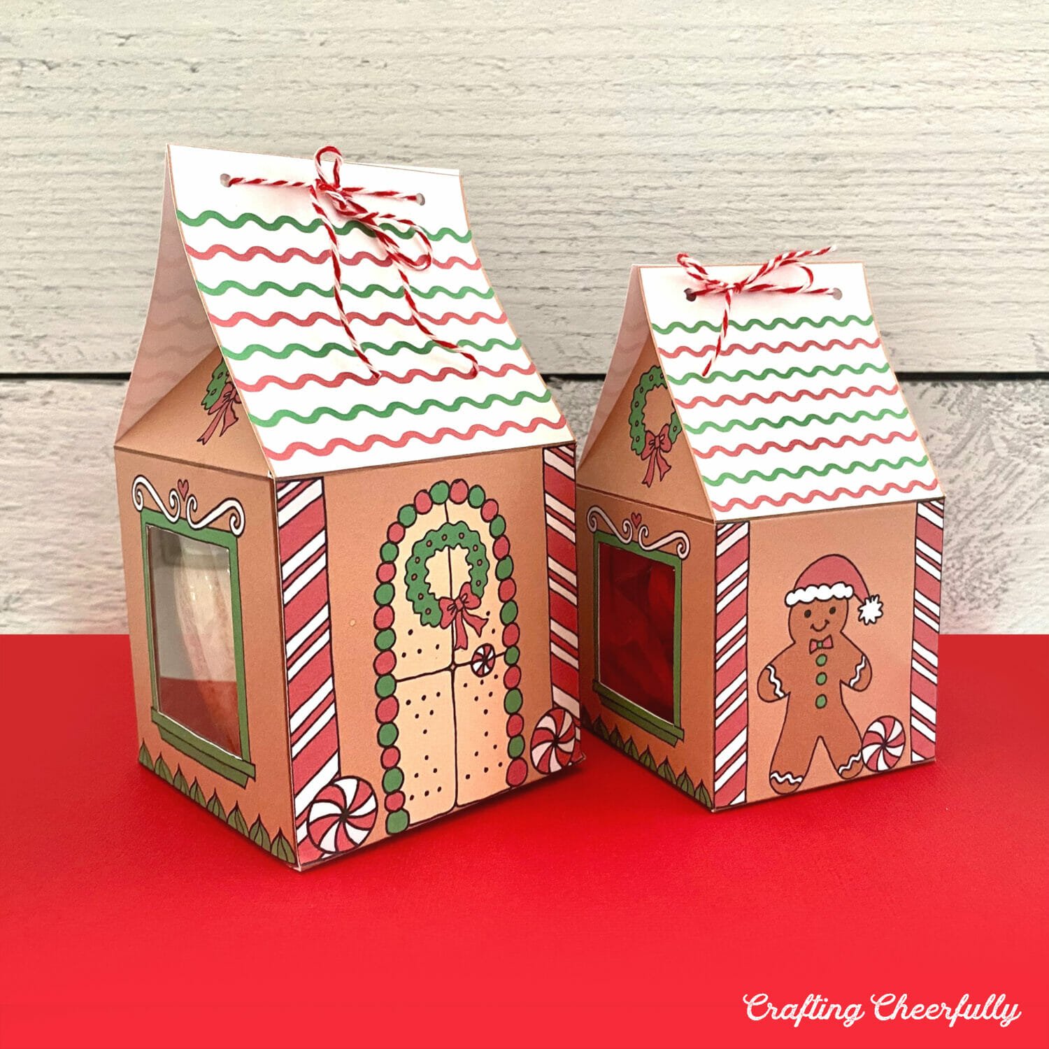 Two gingerbread house treat boxes sit on a red table.