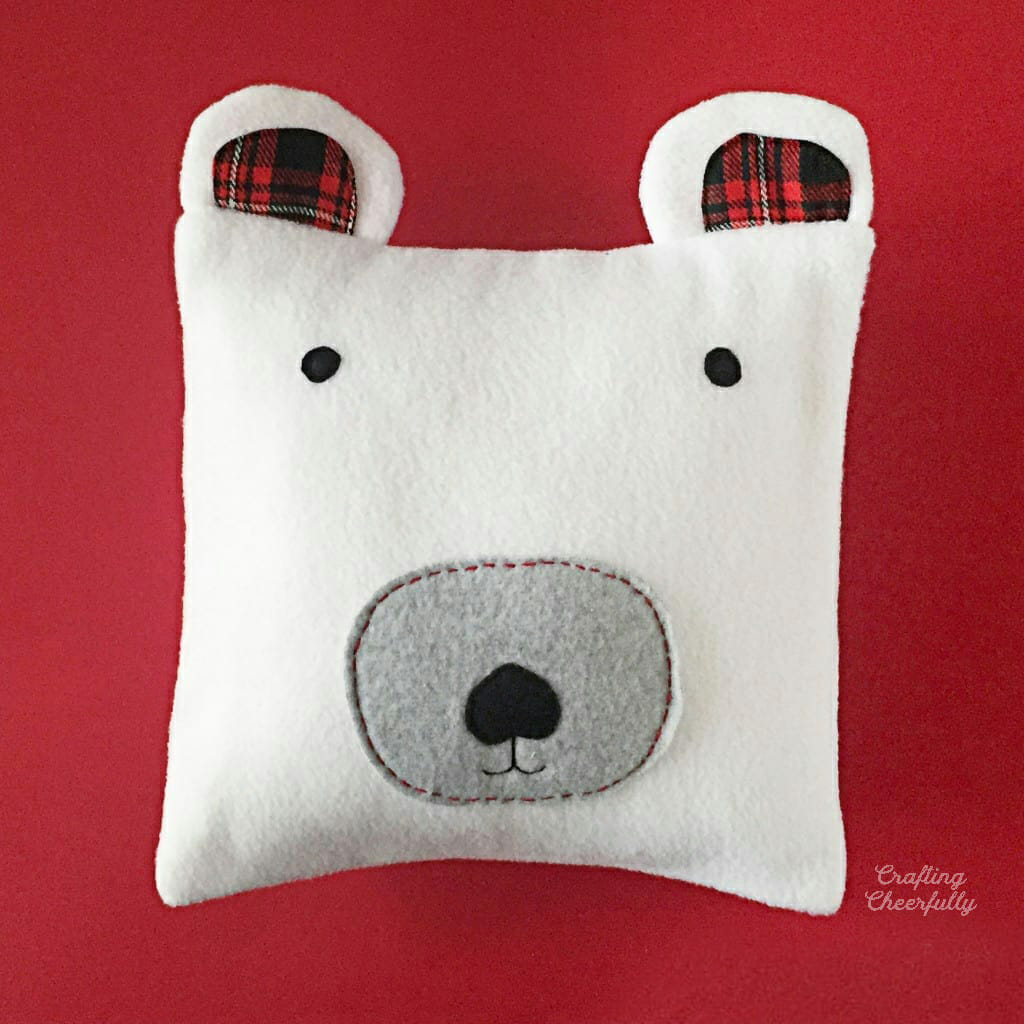 A white fleece polar bear pillow lays on a red surface.