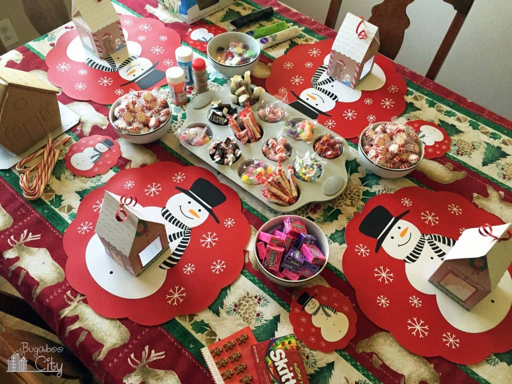 Table set up for decorating gingerbread houses with a muffin tin in the middle filled with candy and sweets.