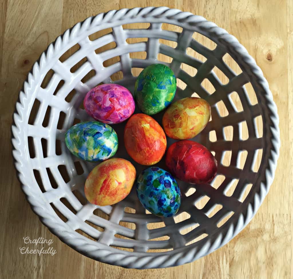 A white basket is filled with tissue paper eggs.