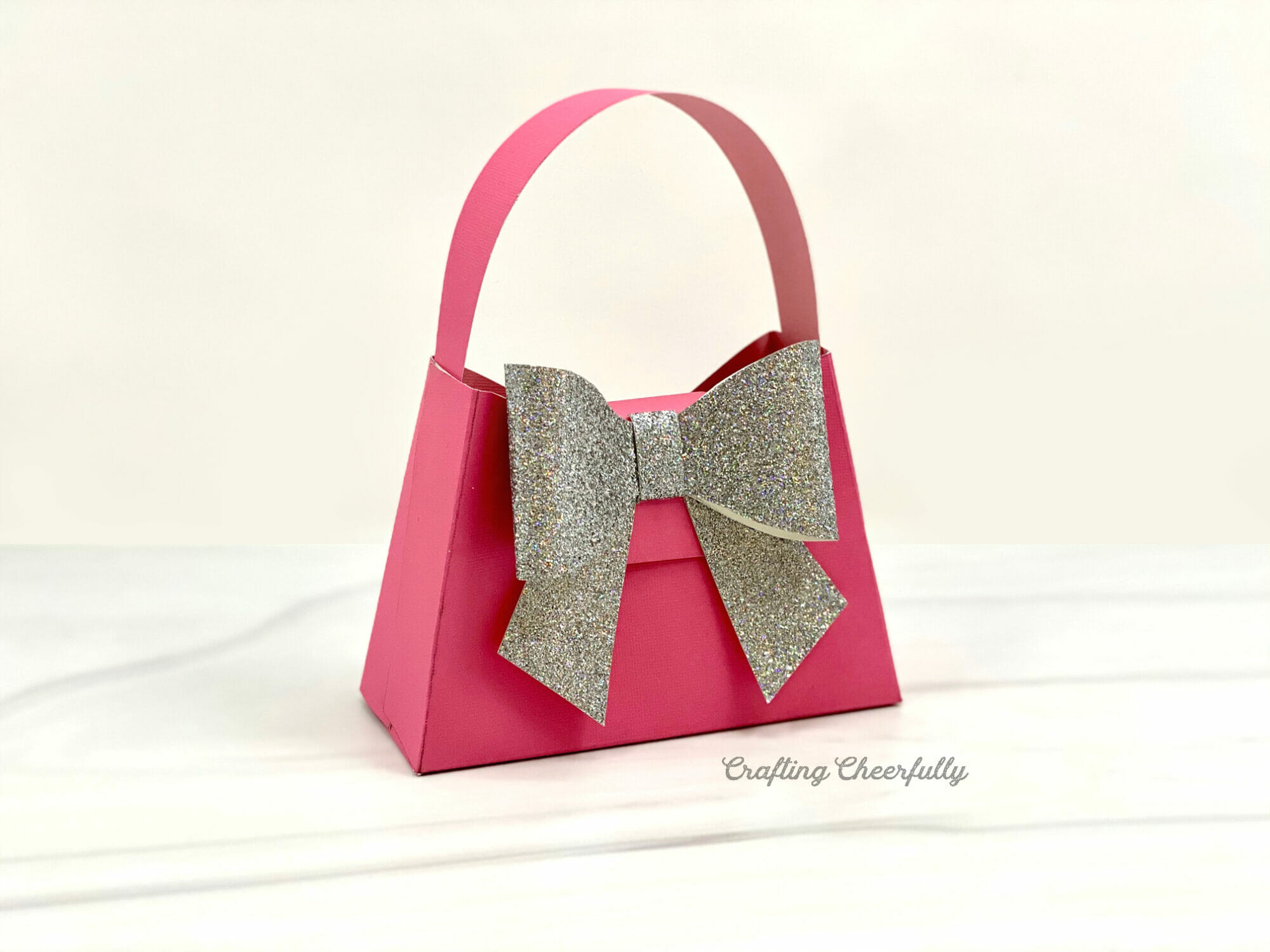 Pink paper purse with large silver bow sits on a marble counter.