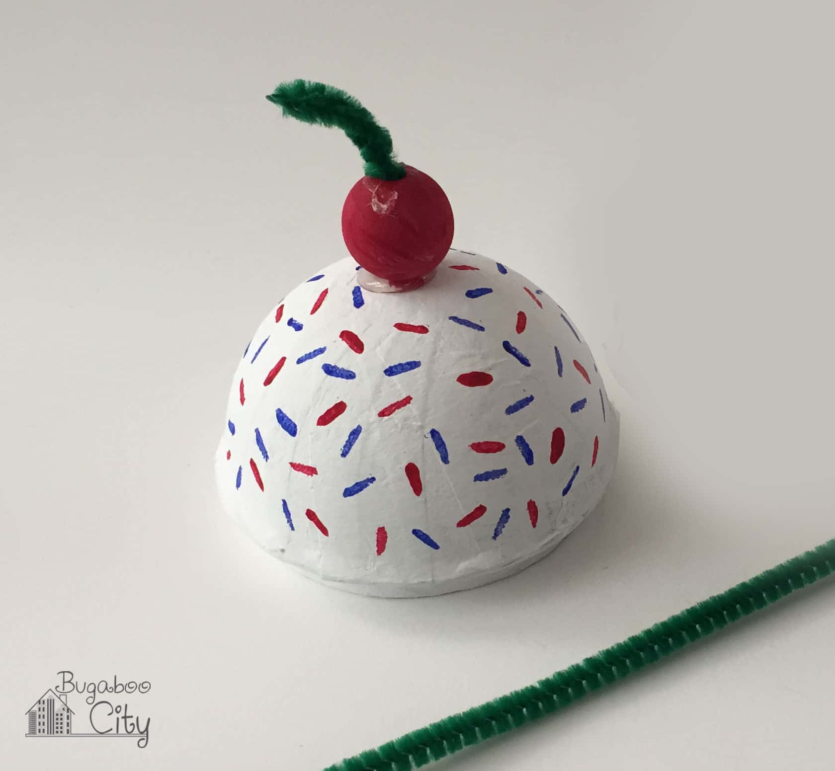 A green pipe cleaner is added to the top of the red wooden cherry.