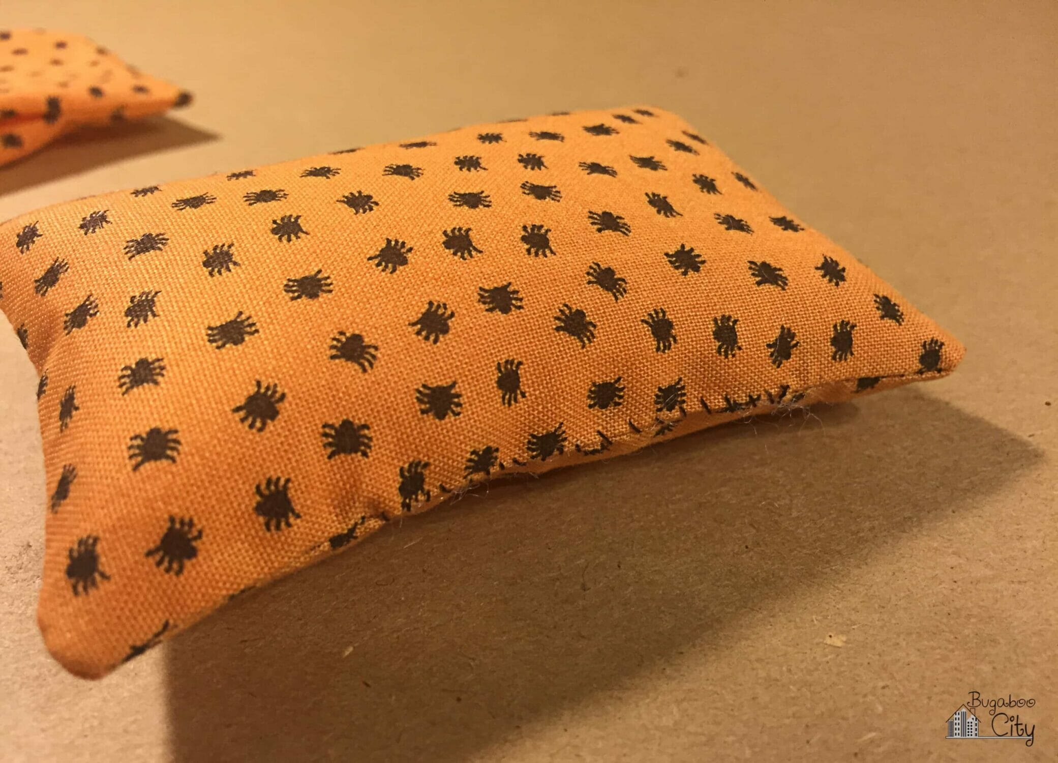 A small pillow made from orange and black spider fabric is stuffed and hand sewn closed.