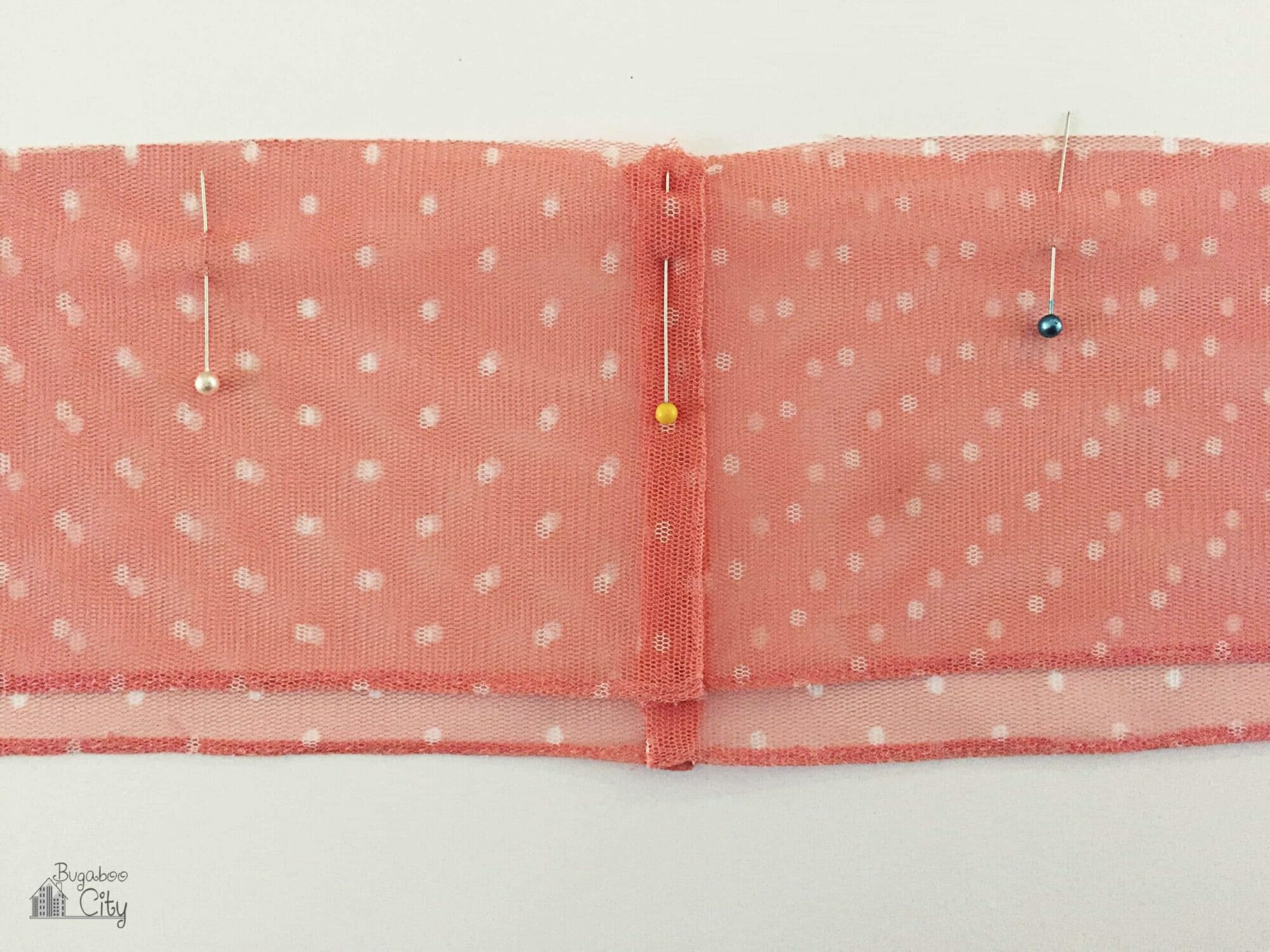 Two layers of pink tulle are stacked with pins holding them along the top edges.