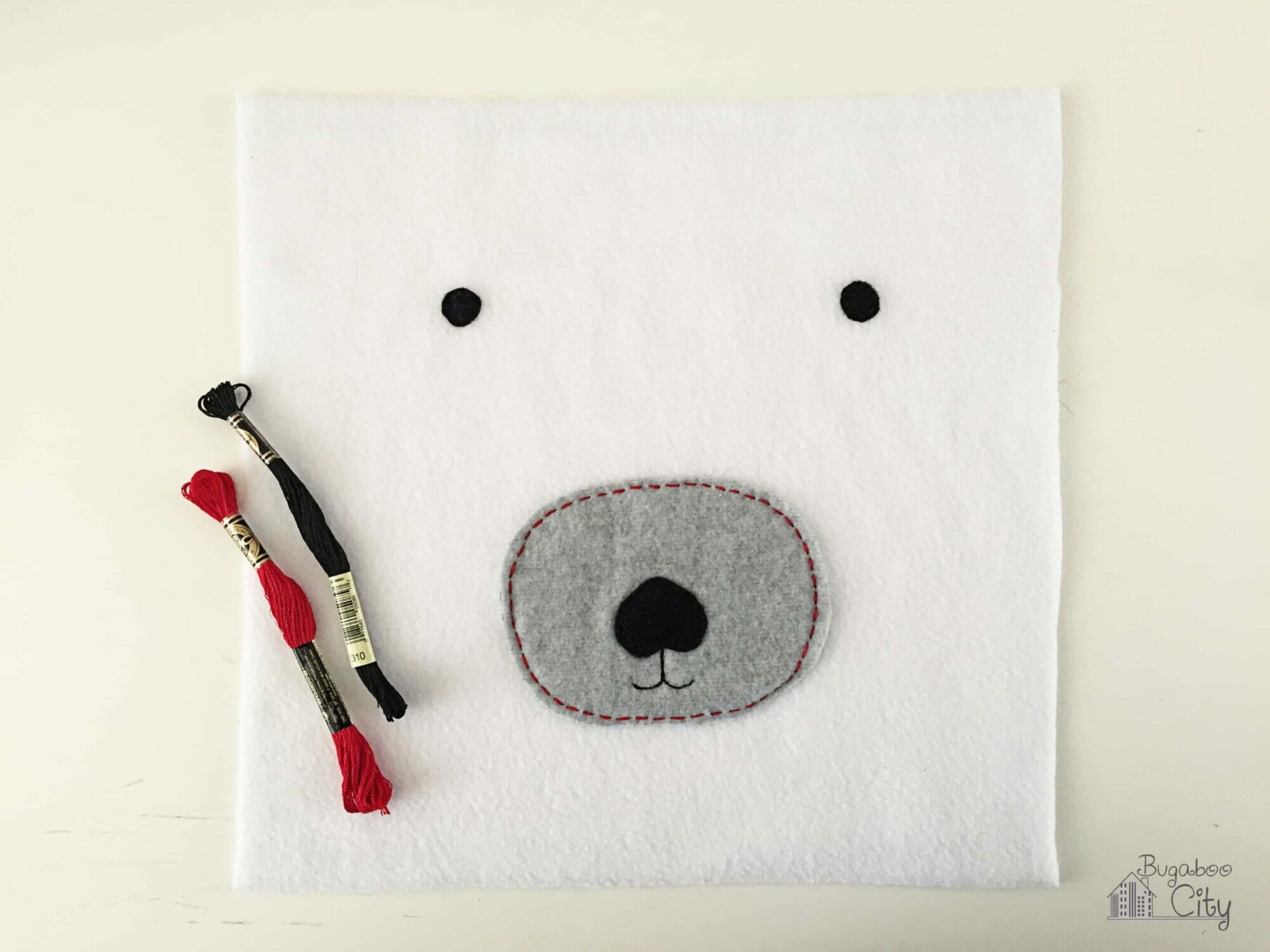 White fleece square with black felt eyes and a gray fleece snout.