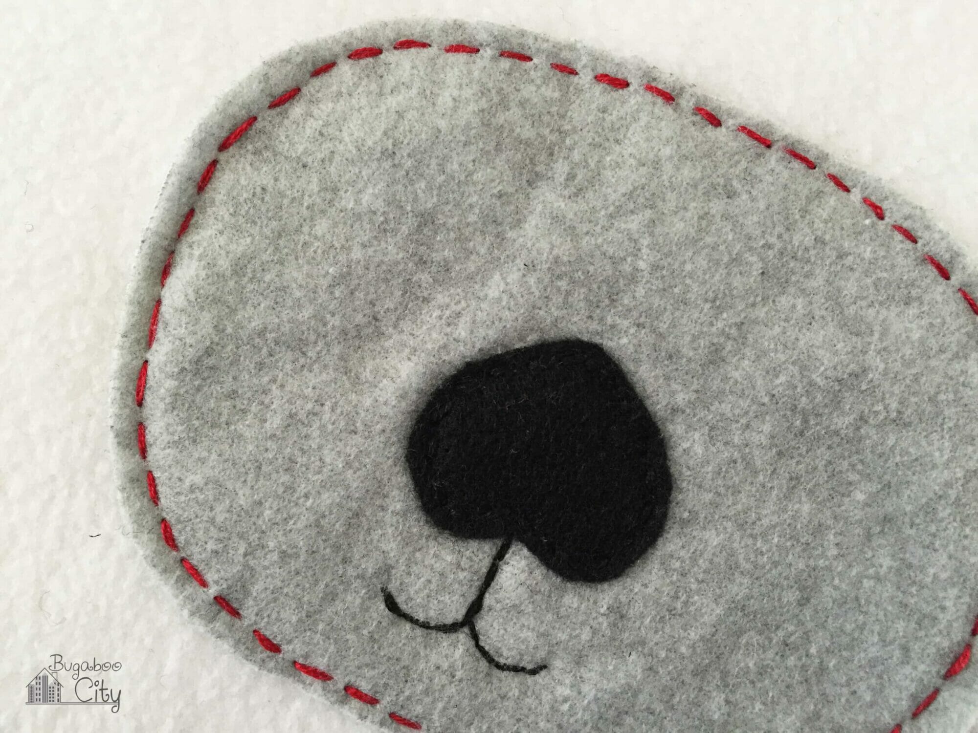 Red handsewn stitches go around the edges of a gray fleece snout.