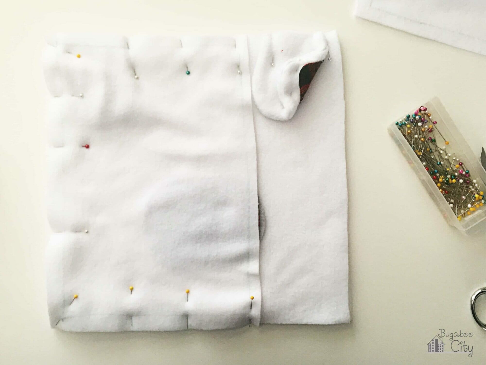 A rectangle piece of white fleece is pinned on top of the polar bear pillow.