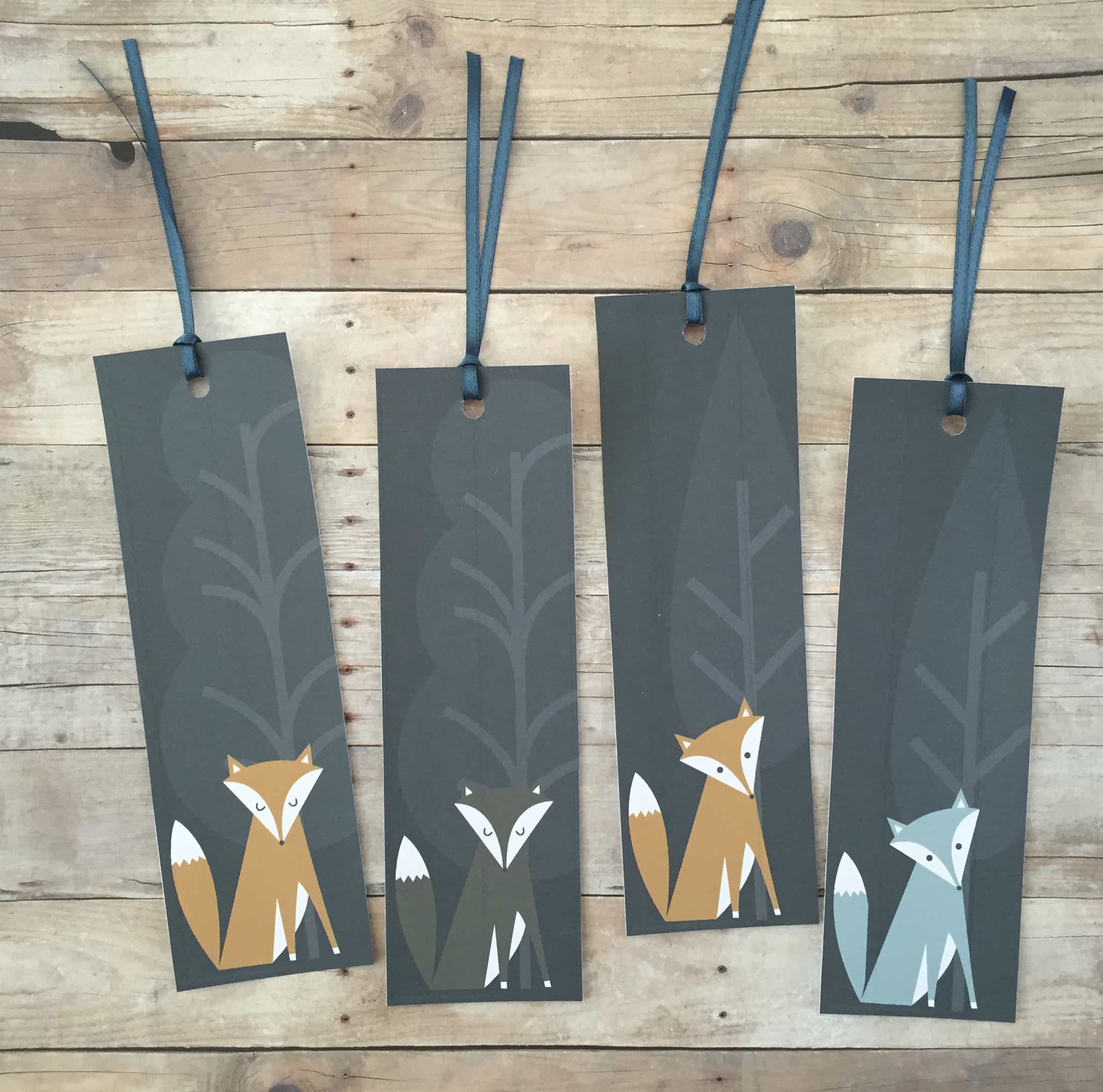 Four fox bookmarks with ribbon laying on a wooden table.