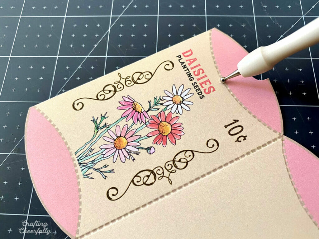 Flower seed treat box is laying on a black self-healing mat with a scoring stylus scoring along the curved edge.