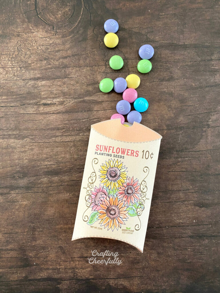 Sunflower treat box laying on a wooden surface with little candy pouring out of it.
