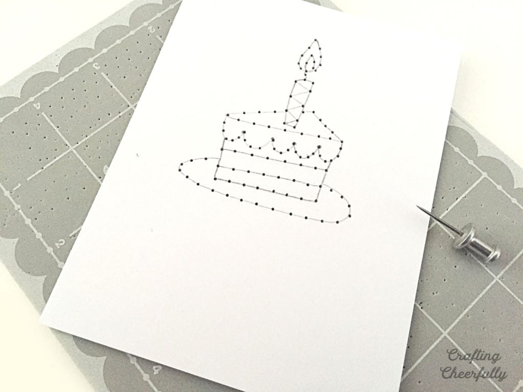 A birthday cake is drawn on a card with pencil; there are holes punched along the lines of the design.