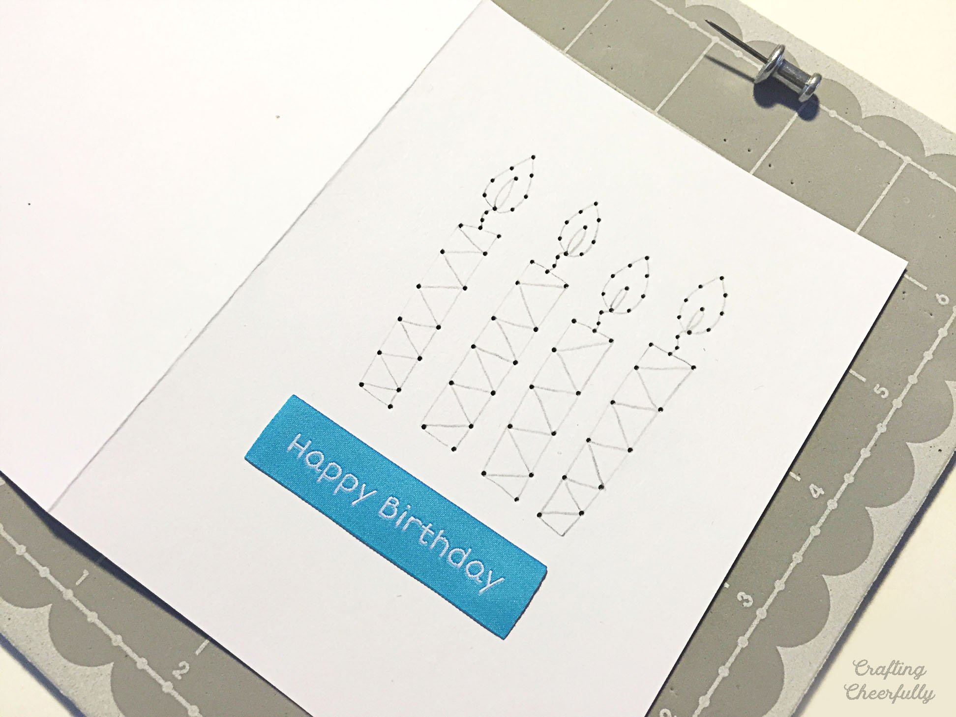Candles are drawn and punched on the front of a white card; a blue fabric label that reads Happy Birthday is underneath.