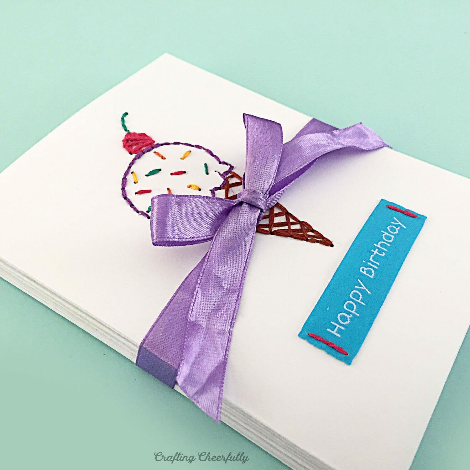 A stack of embroidered birthday cards tied together with a purple ribbon.