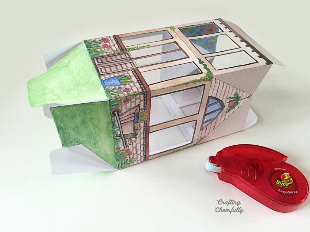 A printed paper greenhouse is folded and taped together.