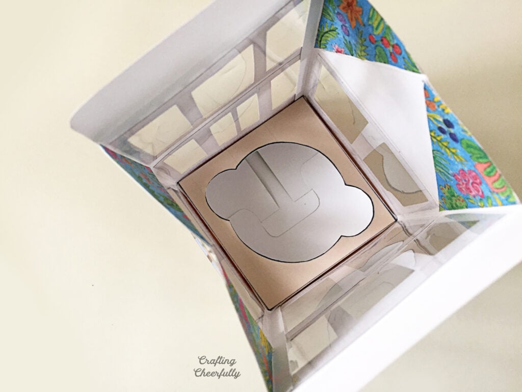 Printed paper greenhouse treat box sits on a white surface with an insert to hold cupcakes.