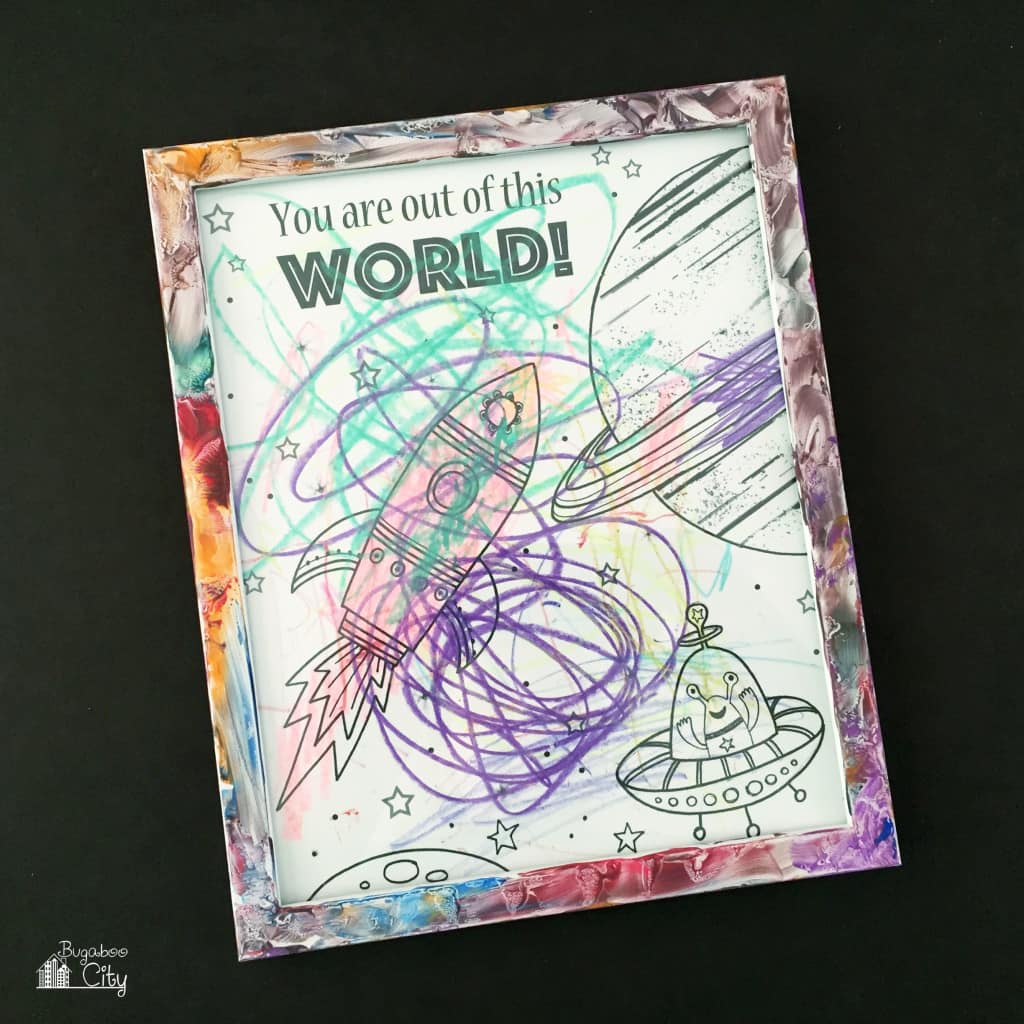 Space Coloring Page colored by a child with crayon framed in a messy finger-painted frame.