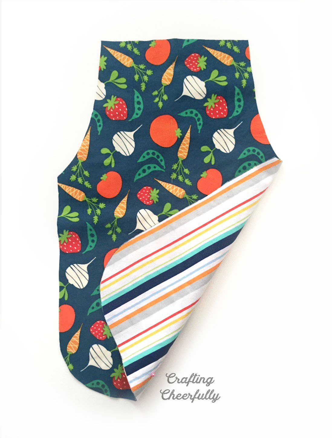 Apron cut from vegetable fabric with bottom edge flipped up to reveal the back of the apron is made using striped fabric.
