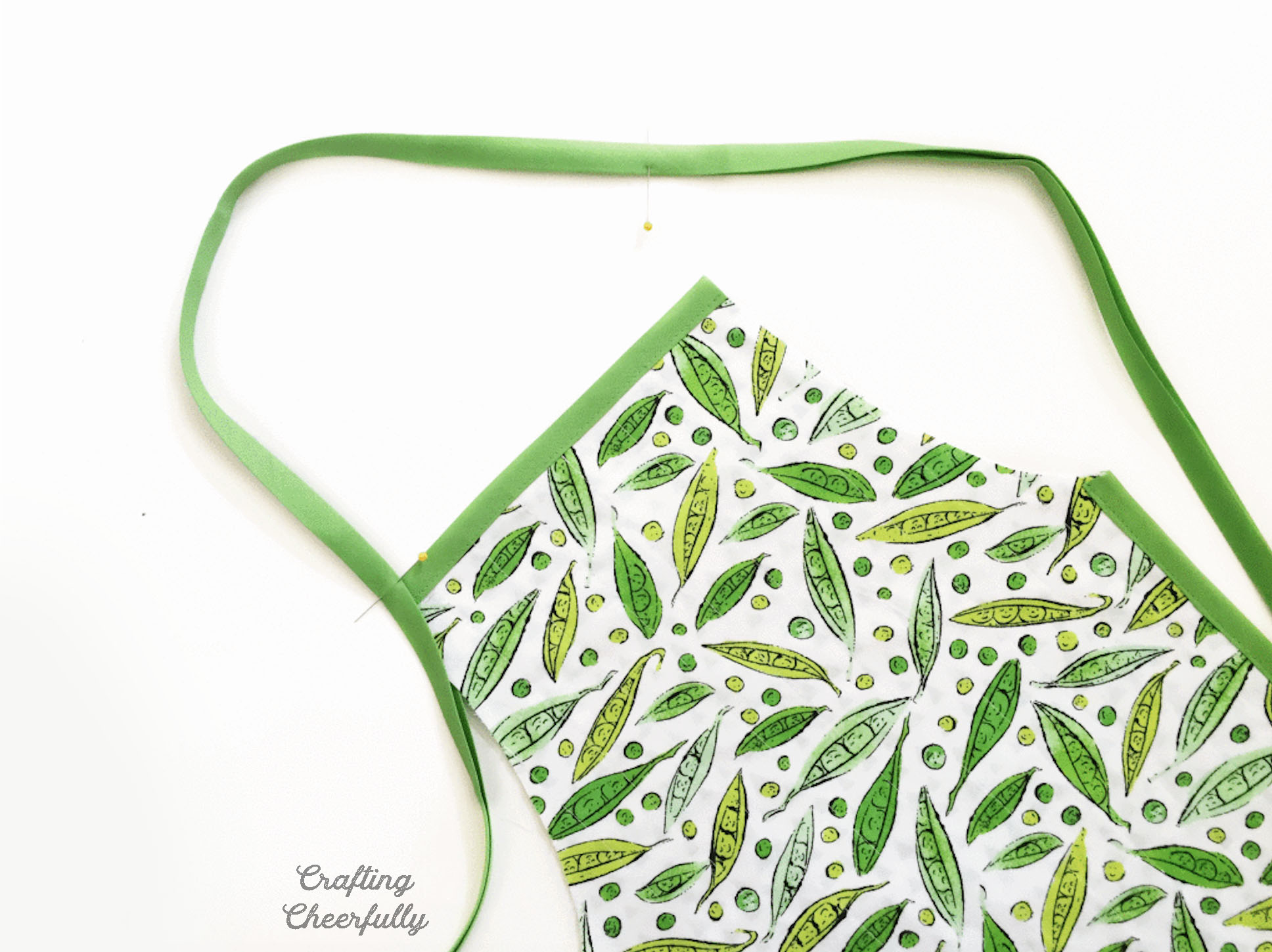 A long length of green bias tape is applied to the apron creating a large neck opening at the top.