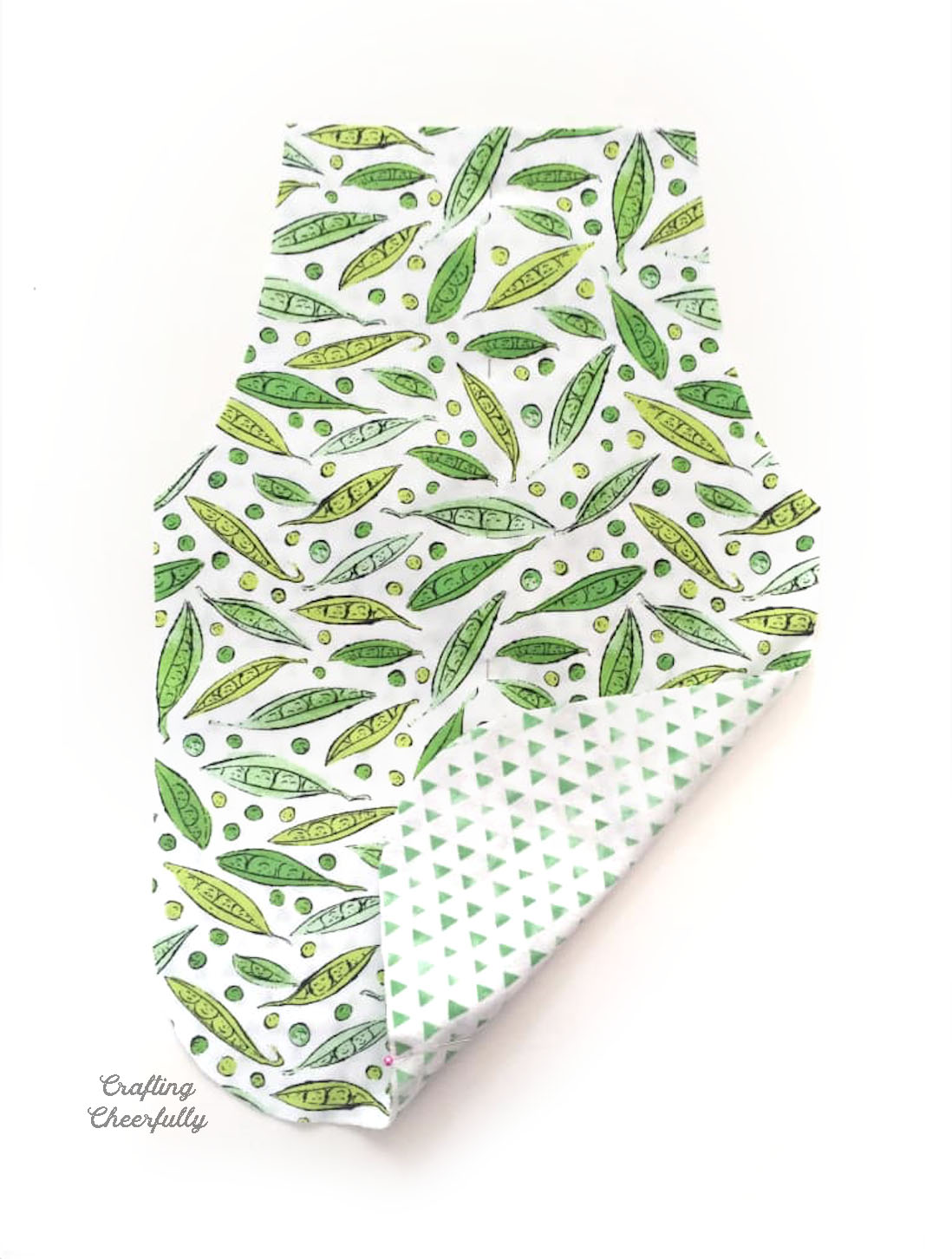 Apron cut from sweet pea fabric with bottom corner lifted up to reveal a green triangle fabric.
