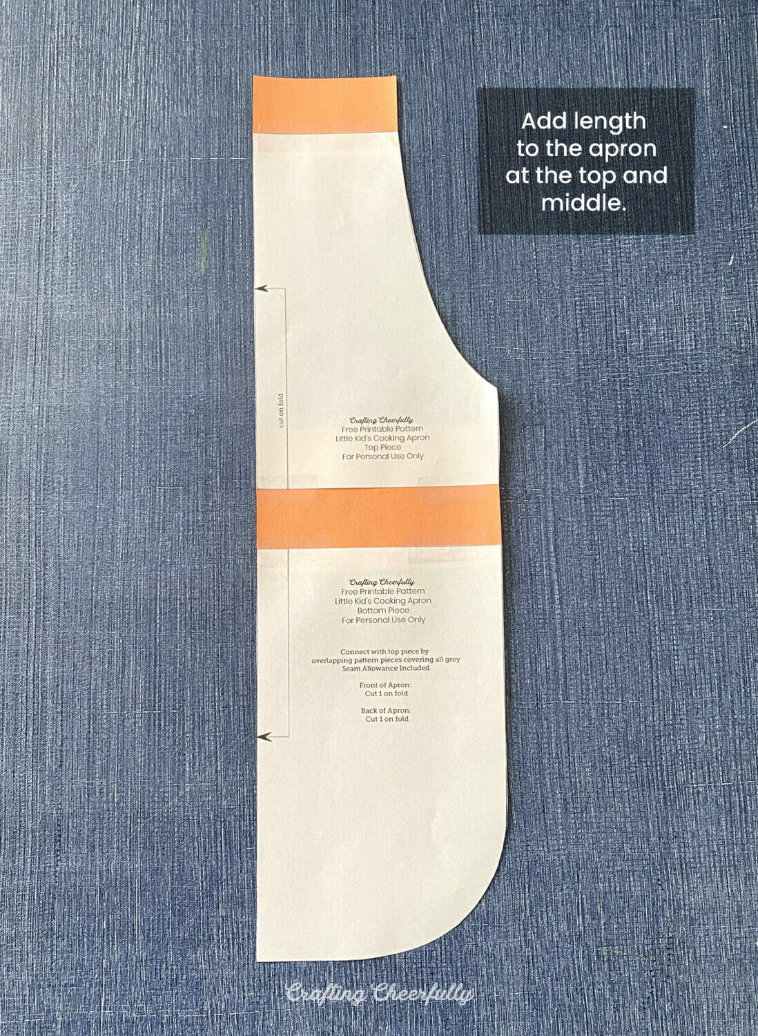 A paper apron pattern with strips of orange paper at the top and in the middle lays on a blue surface.