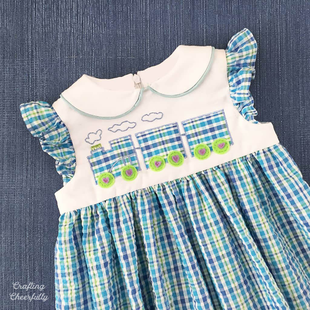 Blue plaid toddler dress with a train applique on the front.