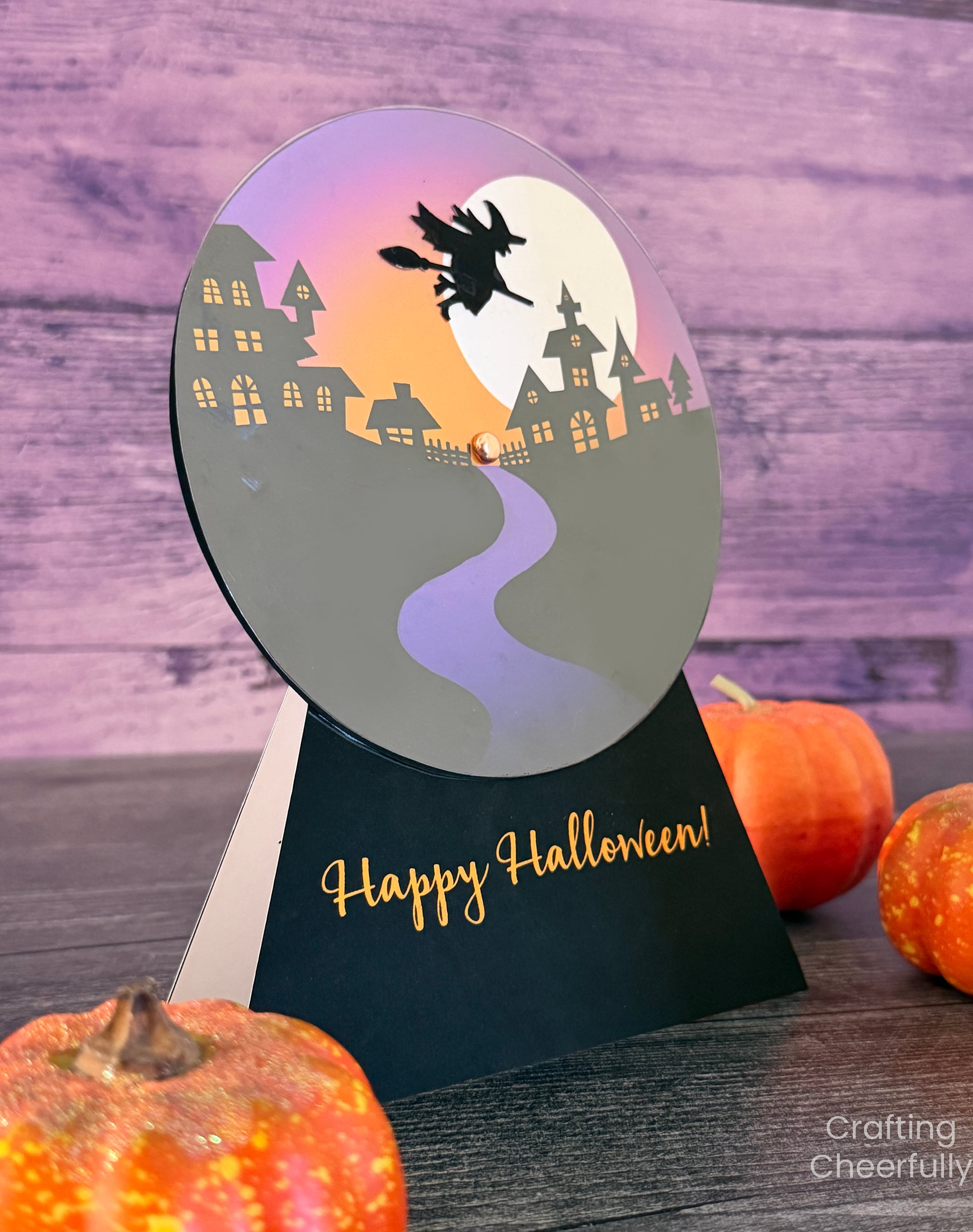 Halloween snow globe card sits on a black table with small pumpkins.