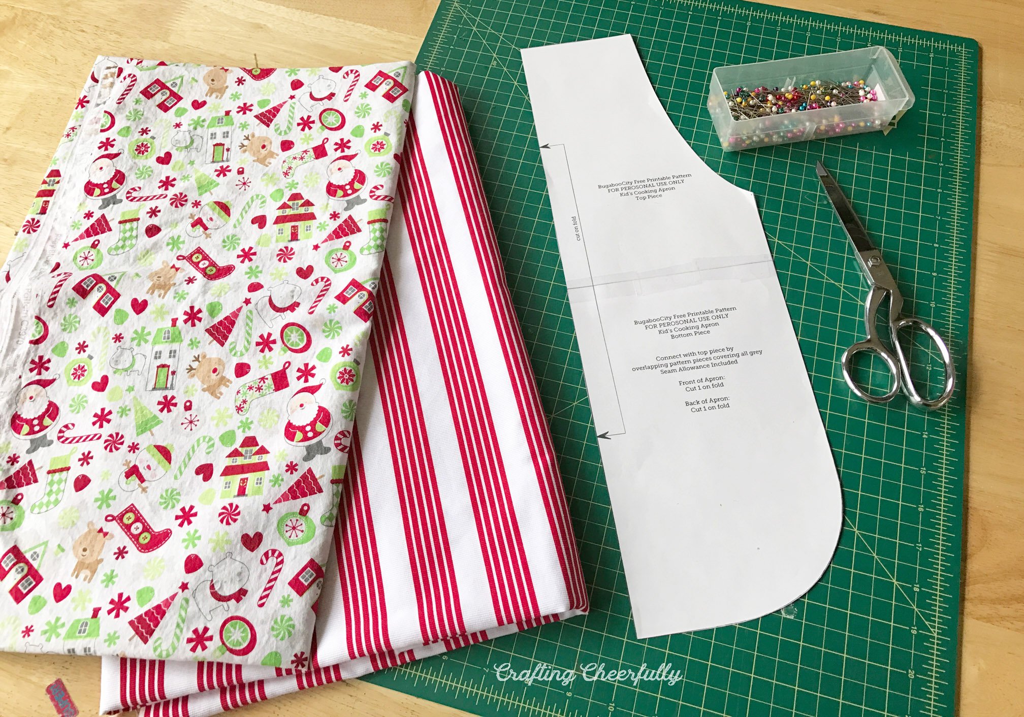 Two fabric prints, one red and white striped, lays next to the pattern piece, scissors and straight pins.