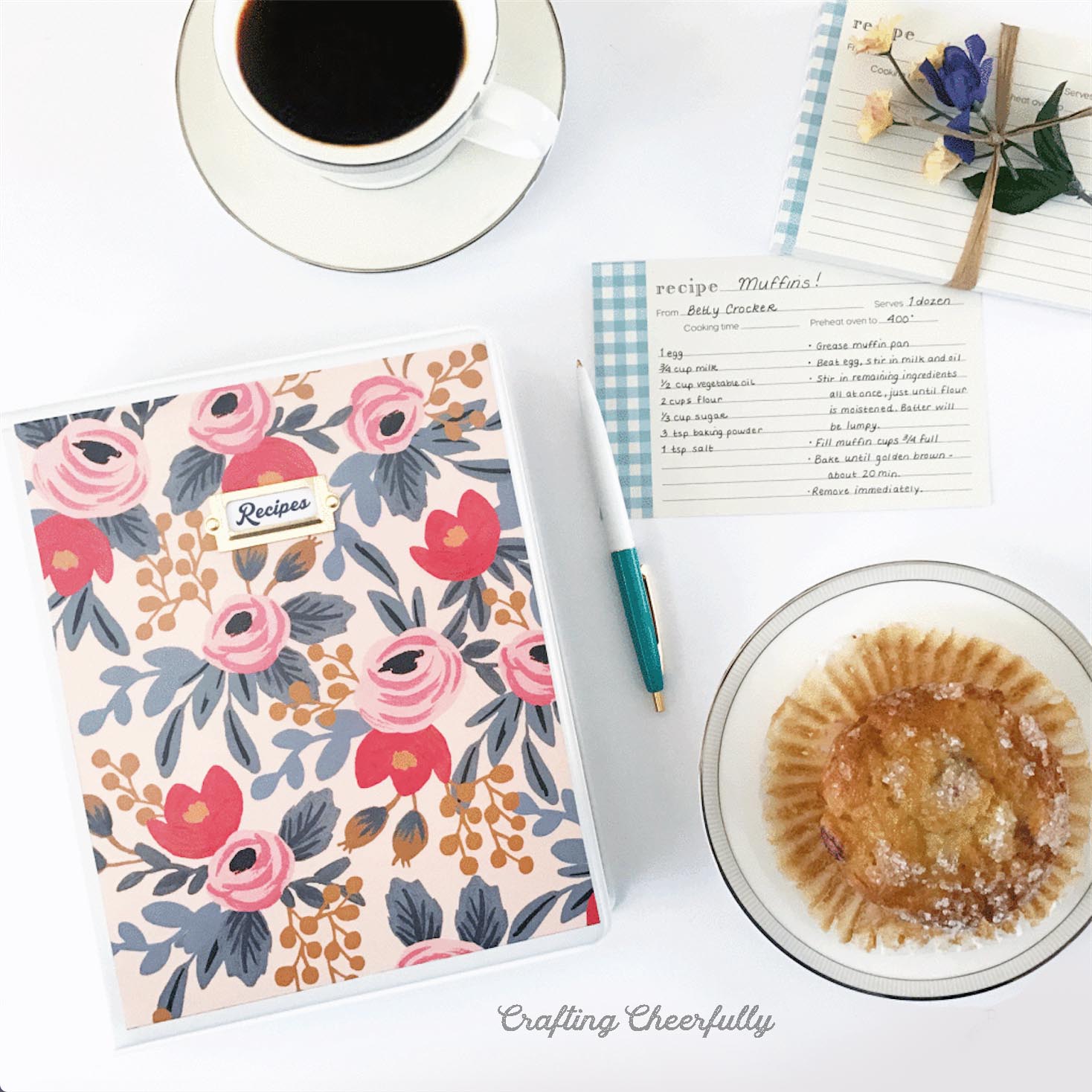 Recipe binder lays next to a cup of coffee, muffin and a group of recipe cards.