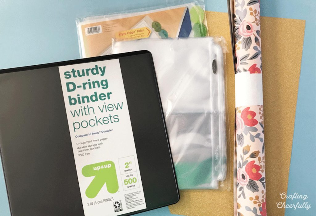 Black D-ring binder, page protectors and a roll of floral paper.