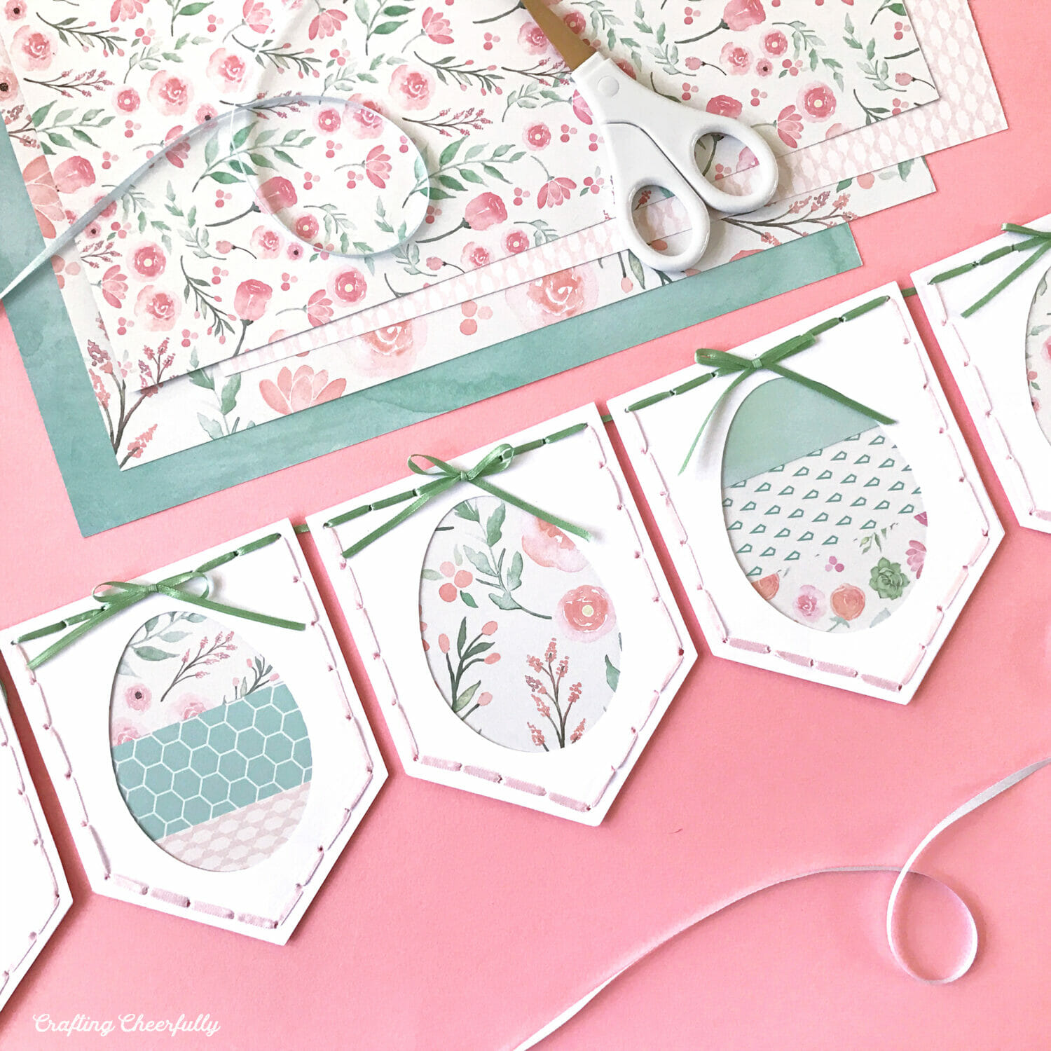 Easter egg banner made from pink, teal and white paper; ribbon is stitched around the edges of each pennant.