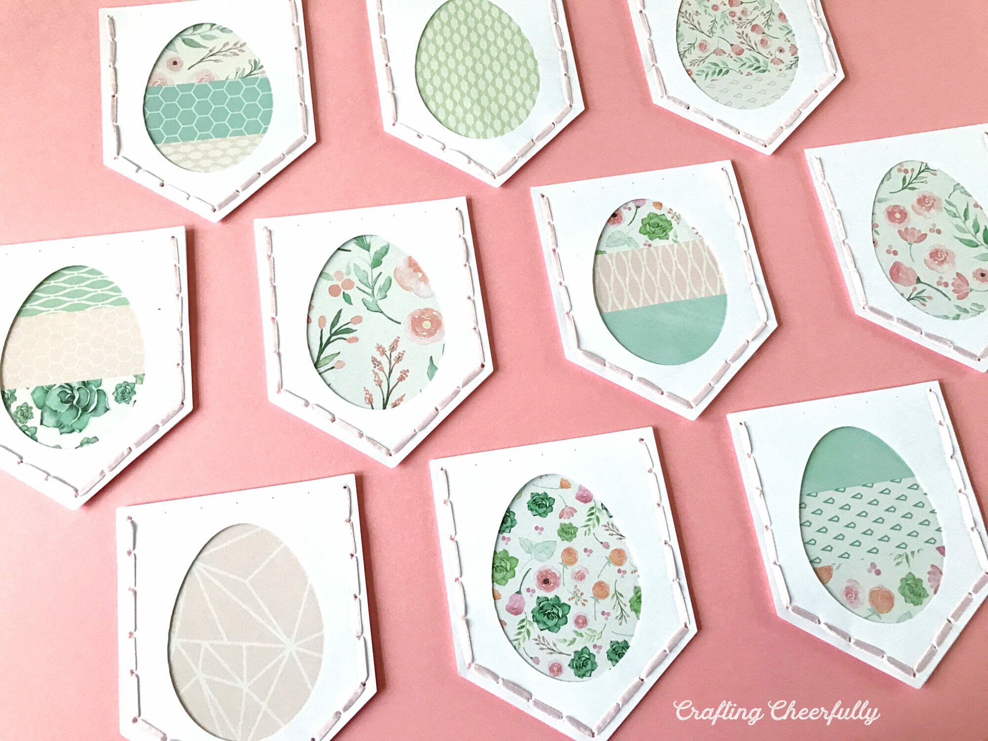 White pennants with decorative srappy eggs on them lay on a pink background.
