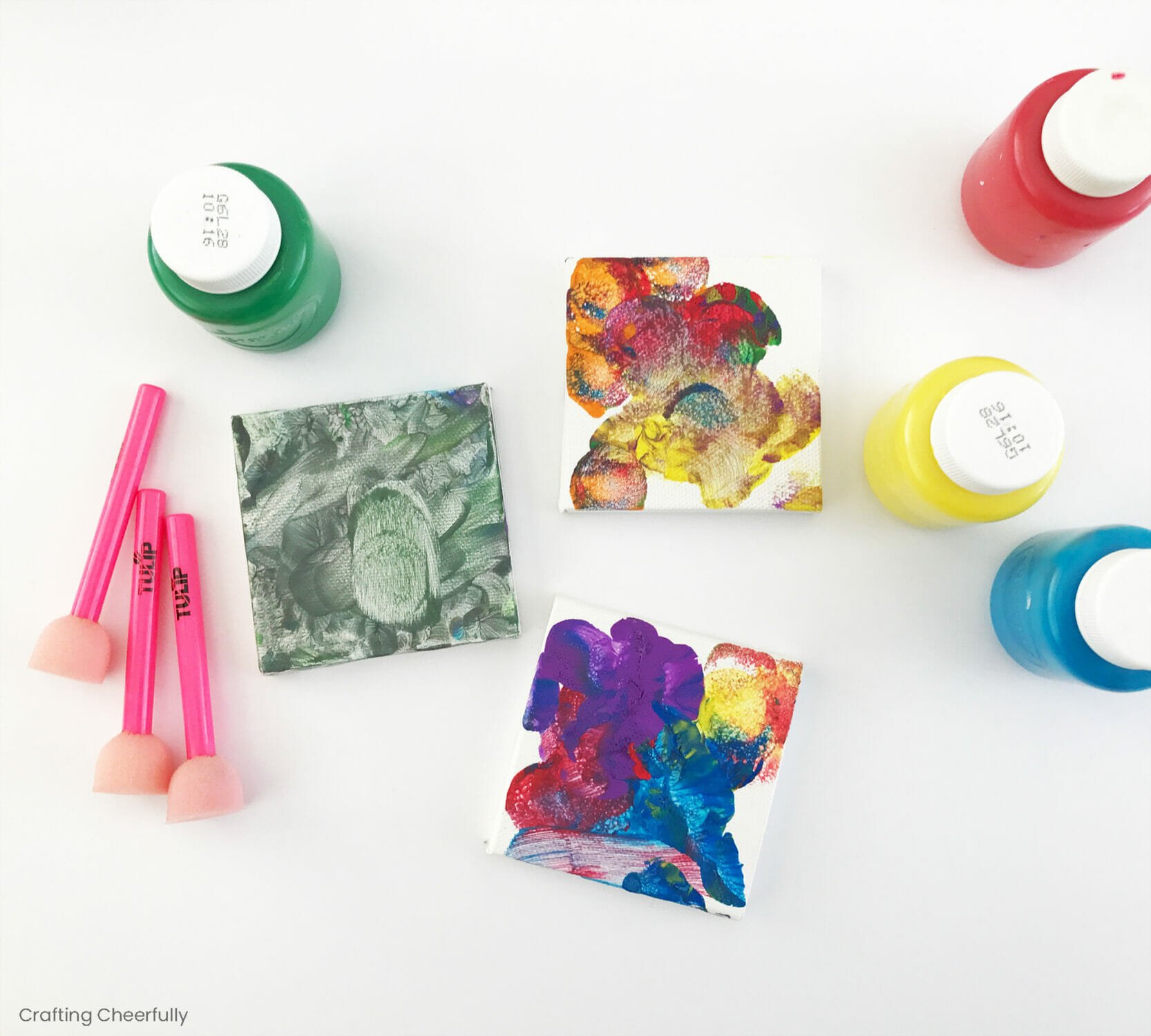 Small square canvases painted with colorful paint lay next to finger paint and pouncers.