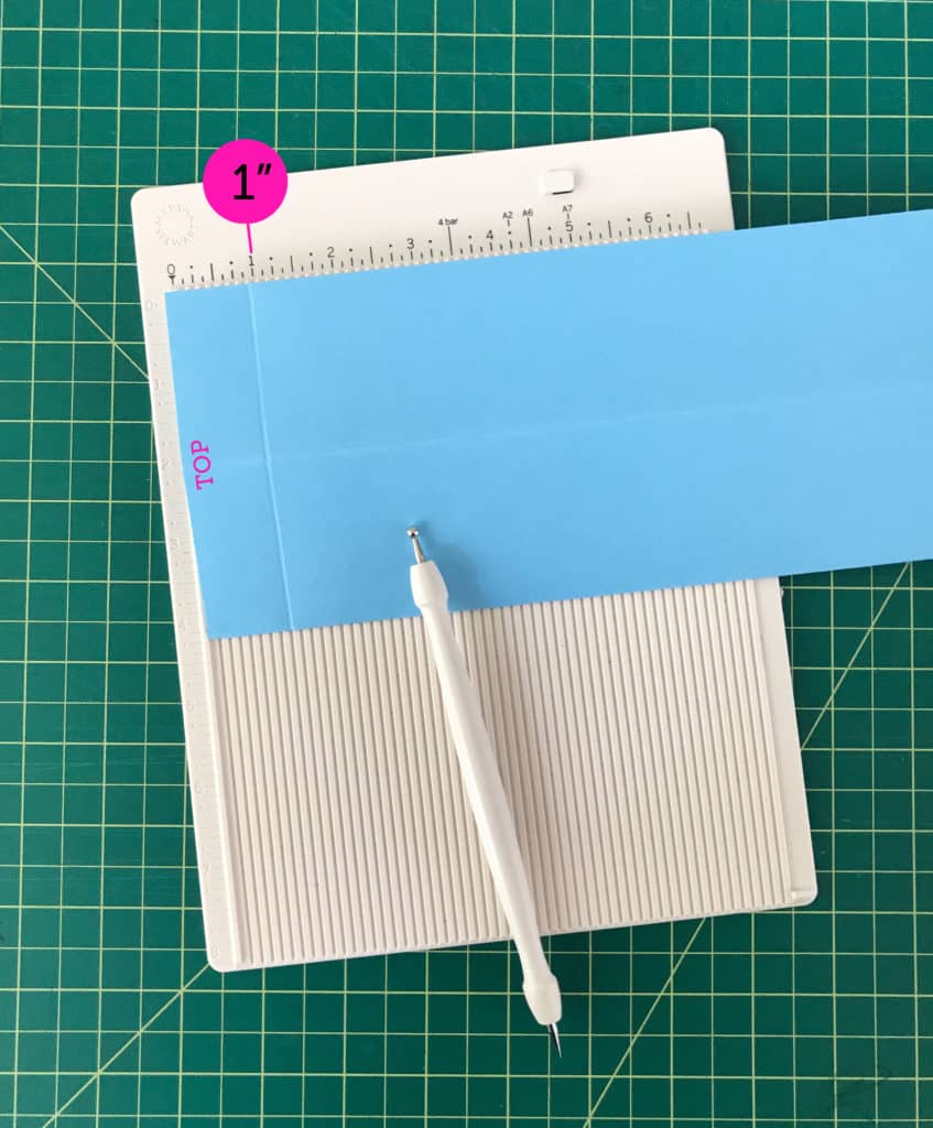 The sheet of blue paper scored along the top edge at one inch.