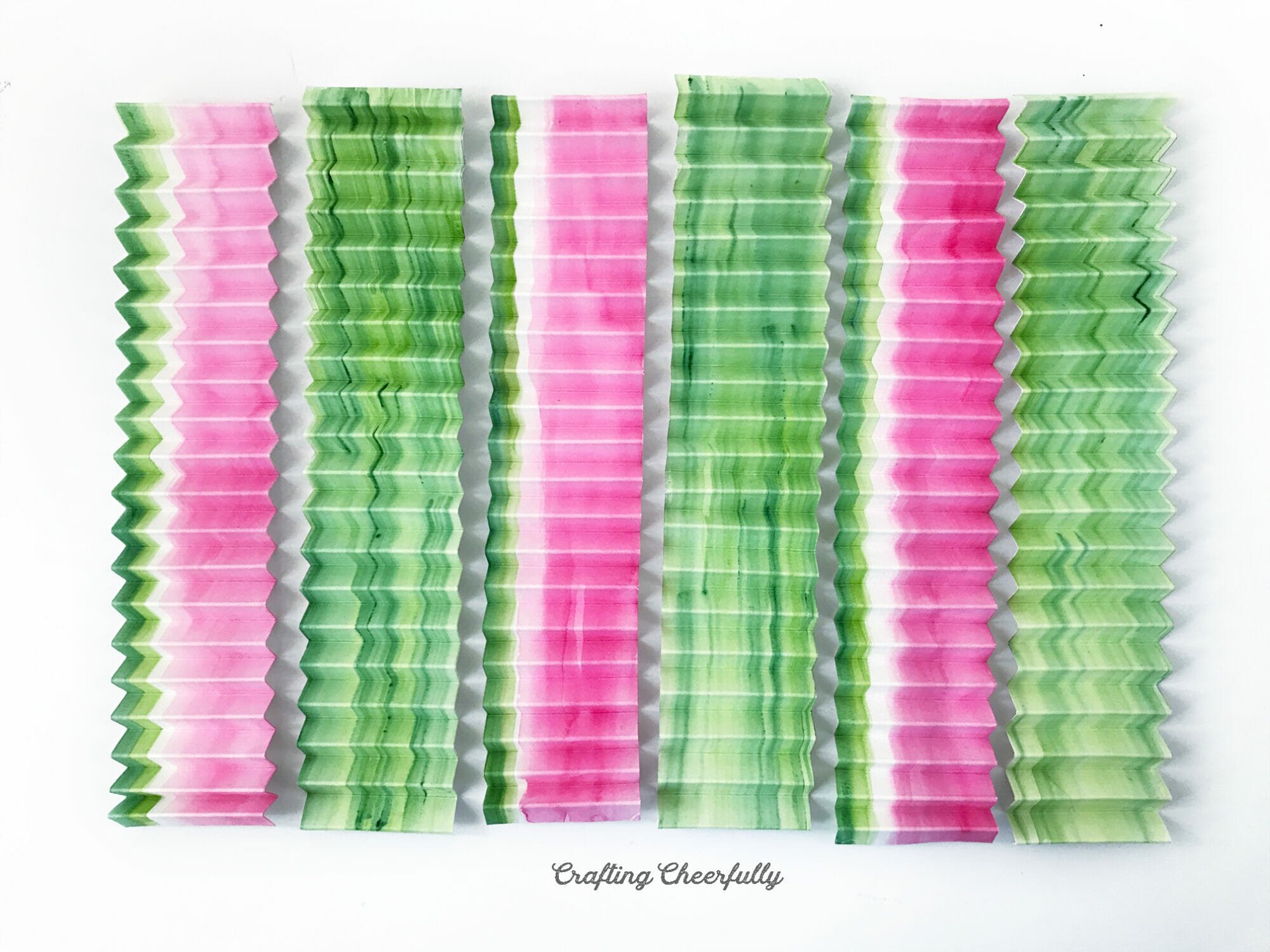 Strips of paper, accordion folded, are lined up on a table top.