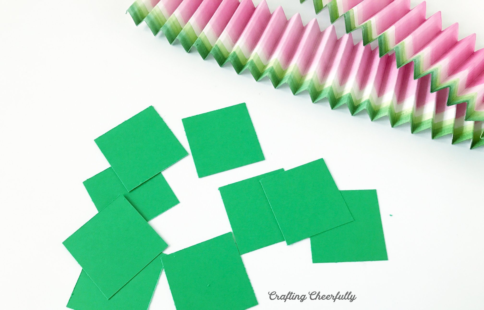 Square pieces of green paper lay next to accordion strips of paper.