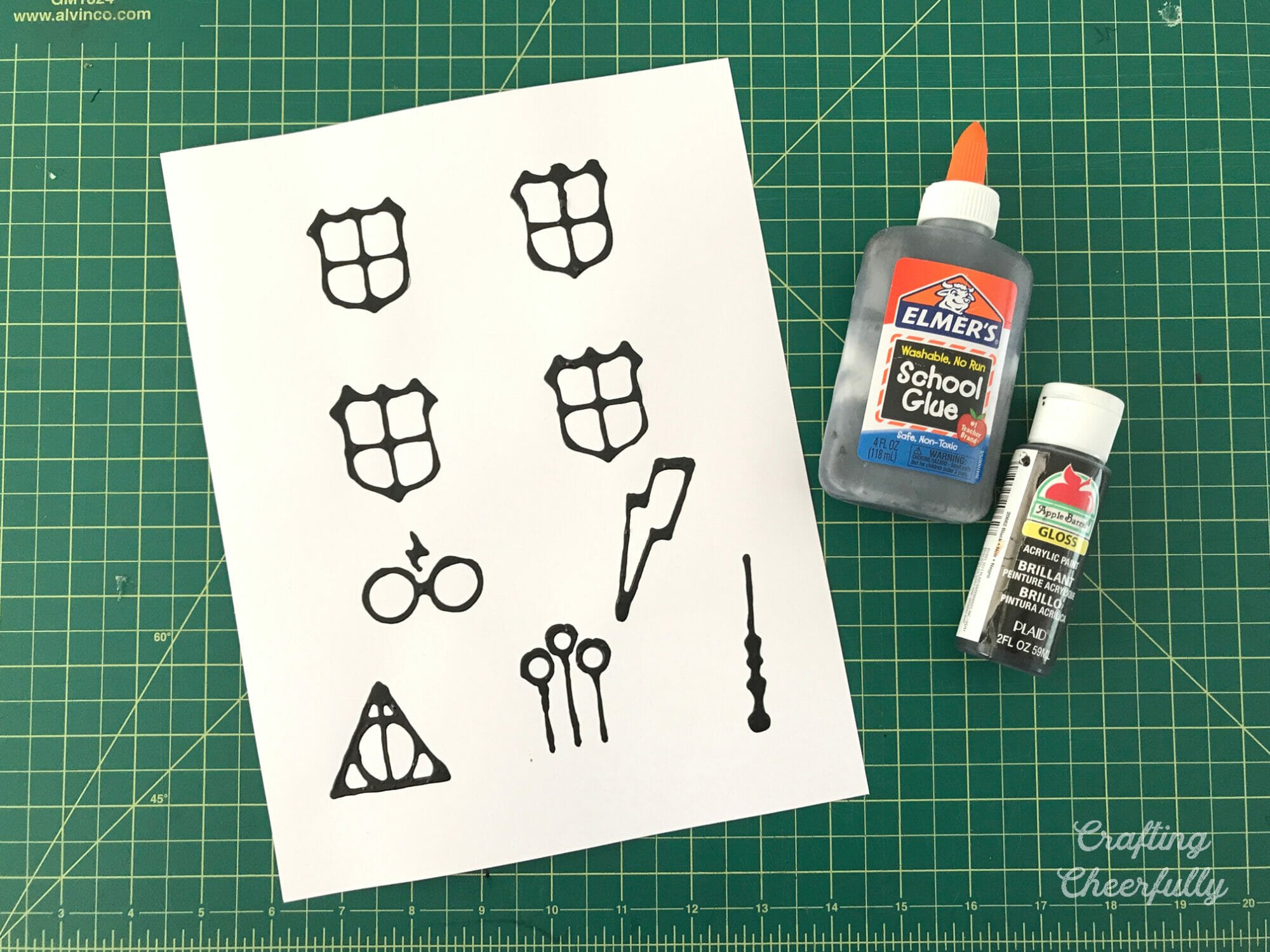Template with designs outlined in black glue lay next to a bottle of black paint and black glue.