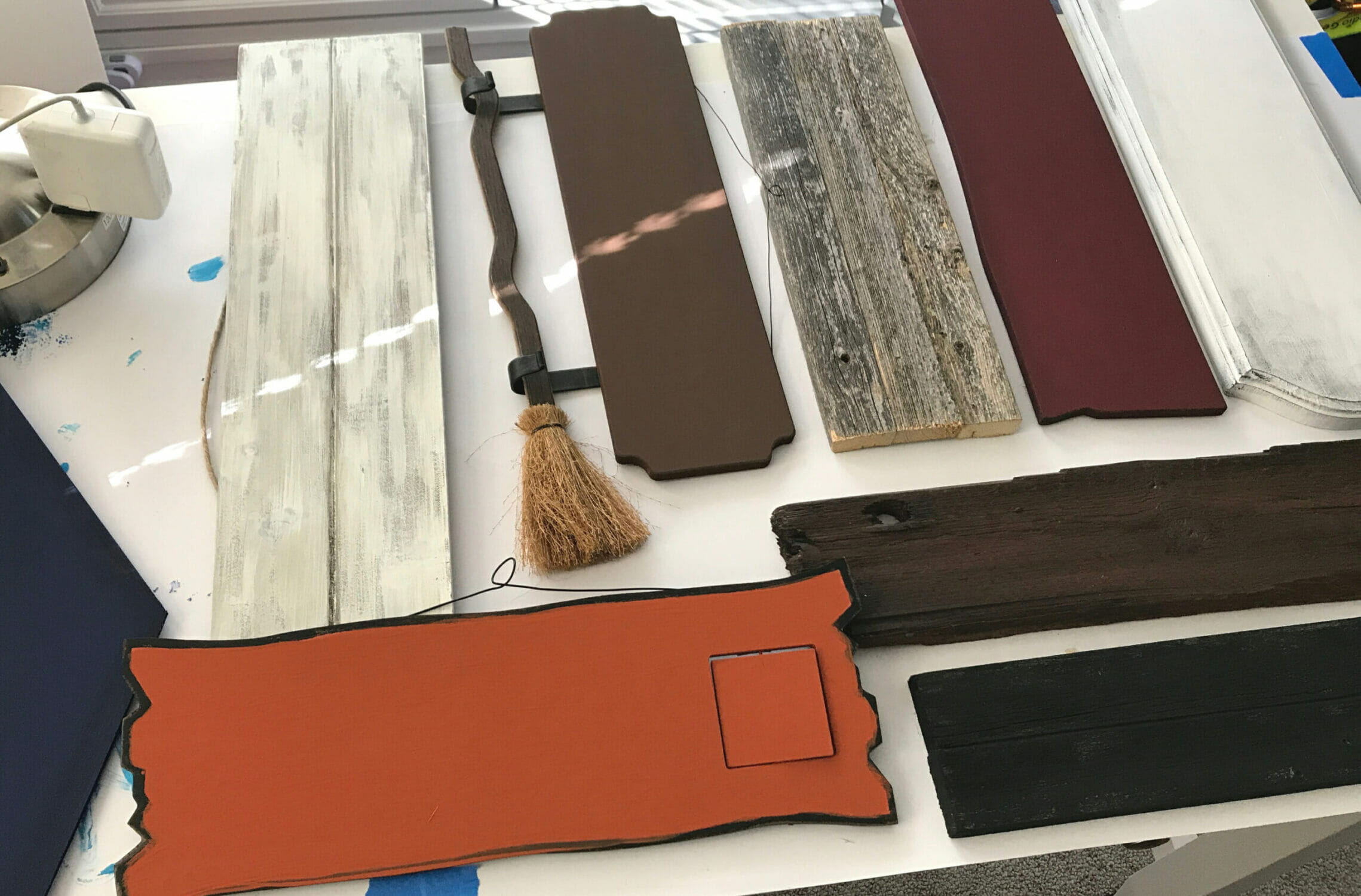 Various wooden signs lay on a table; some are painted, all of them are different sizes.