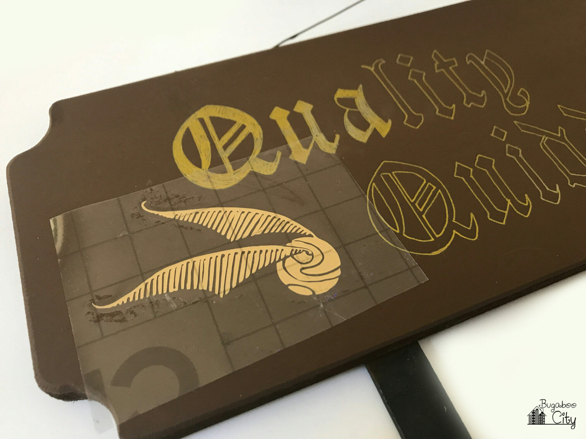 A golden snitch cut from gold vinyl is added to the wooden sign using transfer tape.