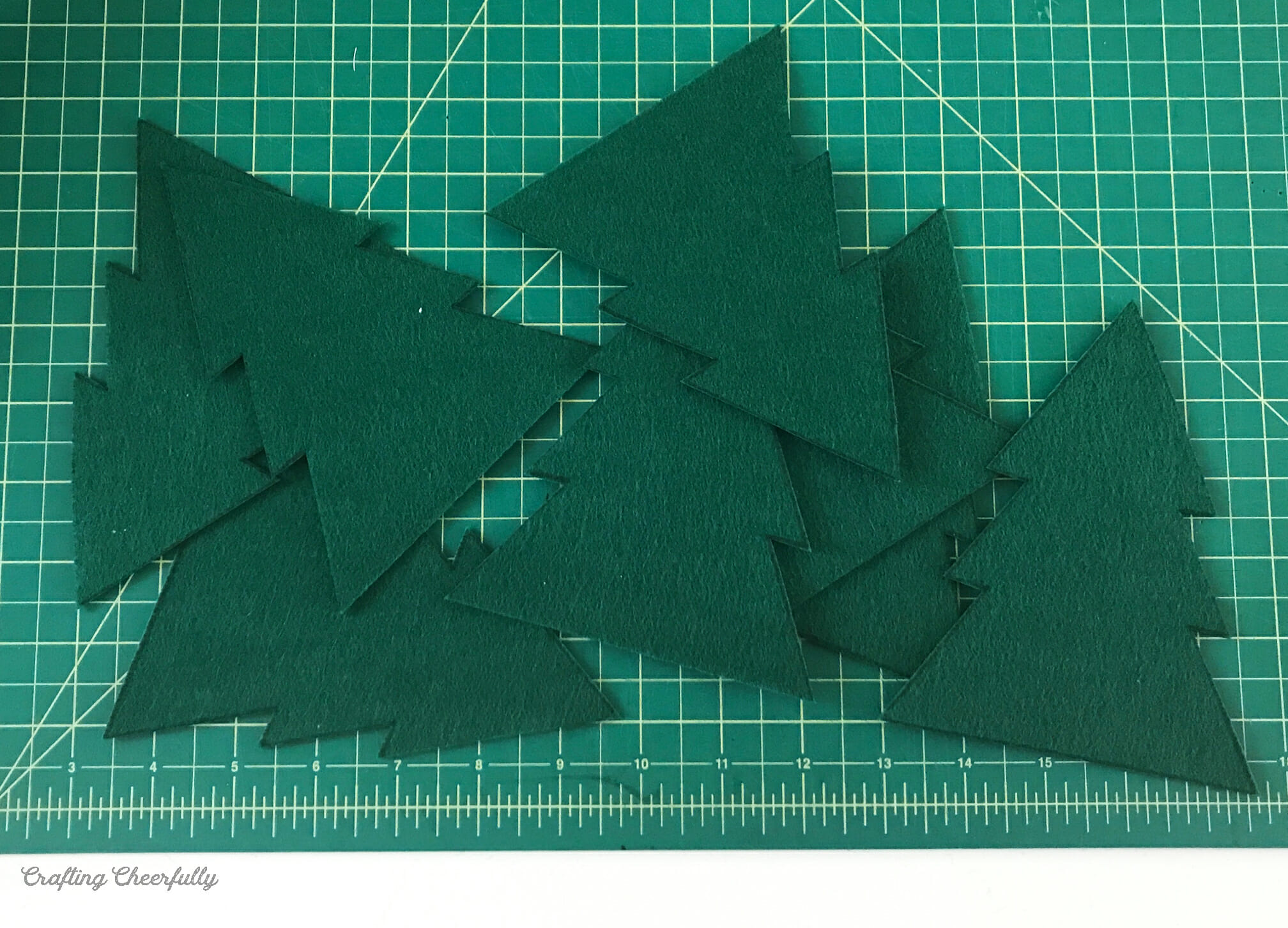 Green felt Christmas trees lay on a green cutting mat.