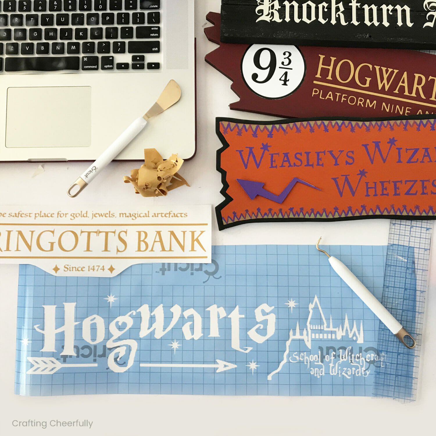 Stencils made from vinyl lay next to finished wooden signs and a laptop.