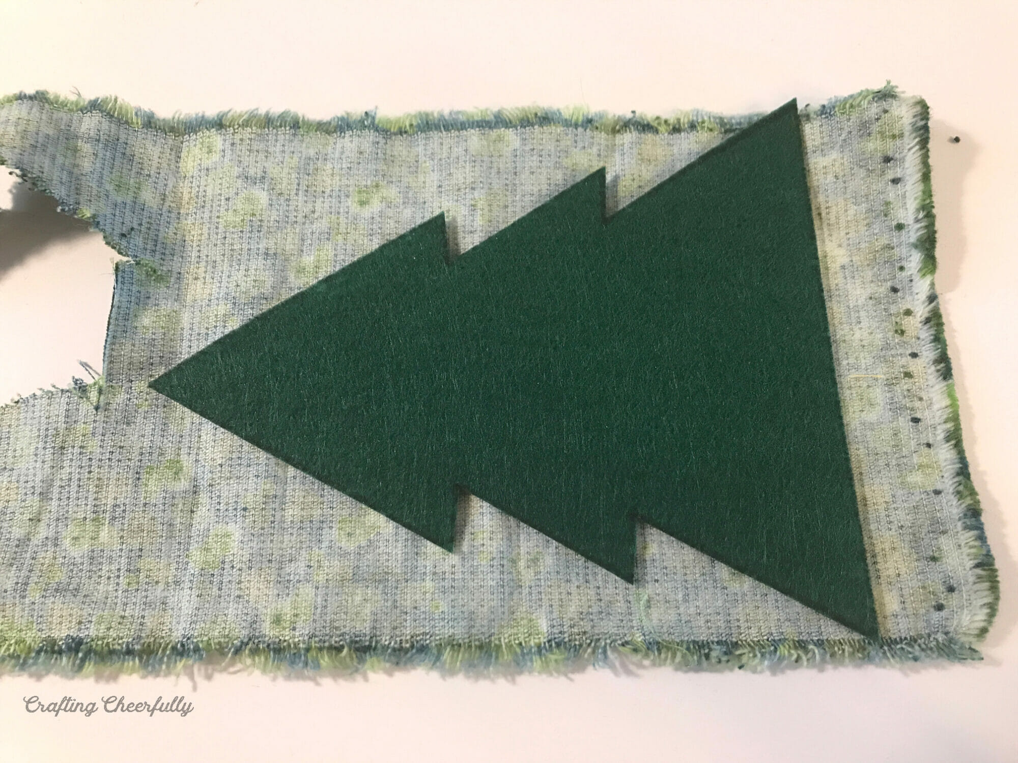 Felt Christmas tree is laid out on a scrap of green wood as a templte.