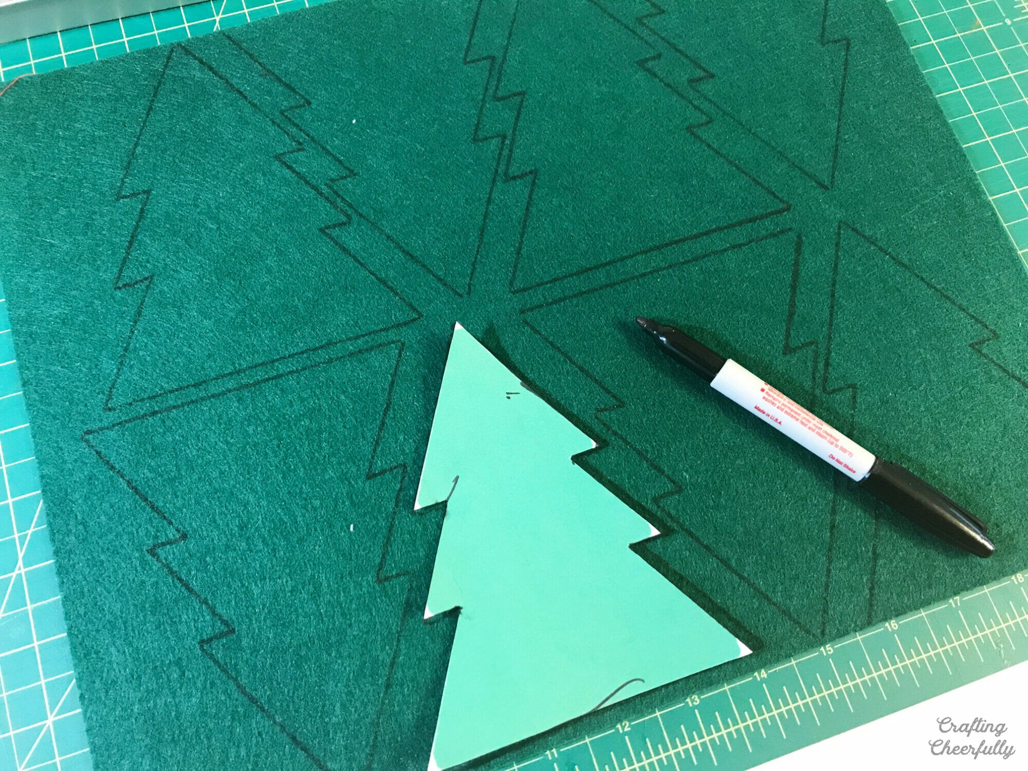 A paper tree template is used to cut Christmas trees from green felt.