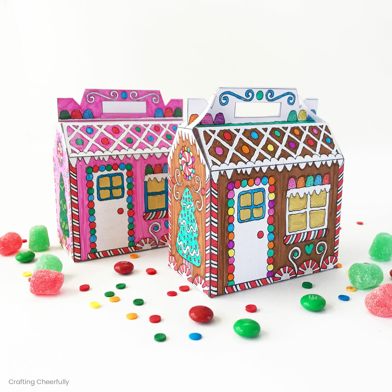 Two gingerbread house boxes that have been colored with marker sit on a table surrounded by candy.