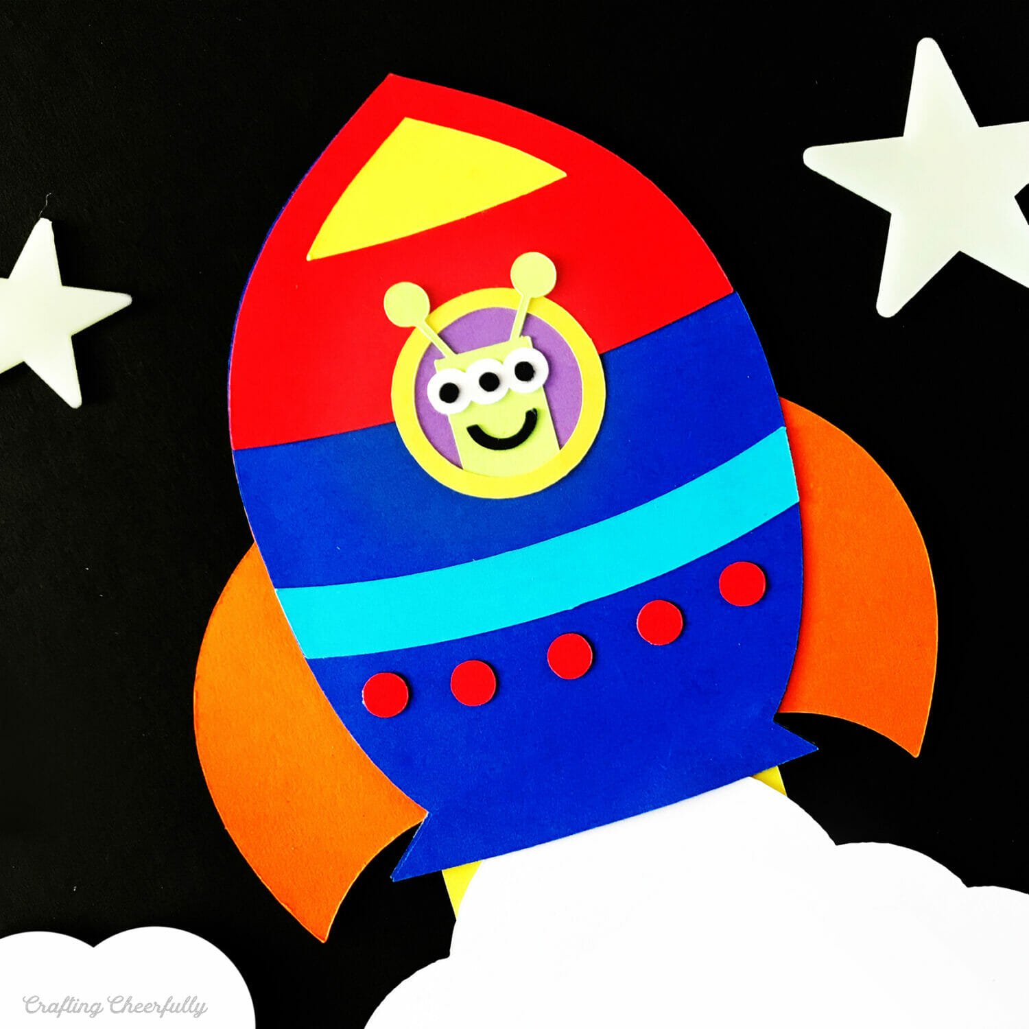 Colorful paper rocket ship card with cute alien in the window.