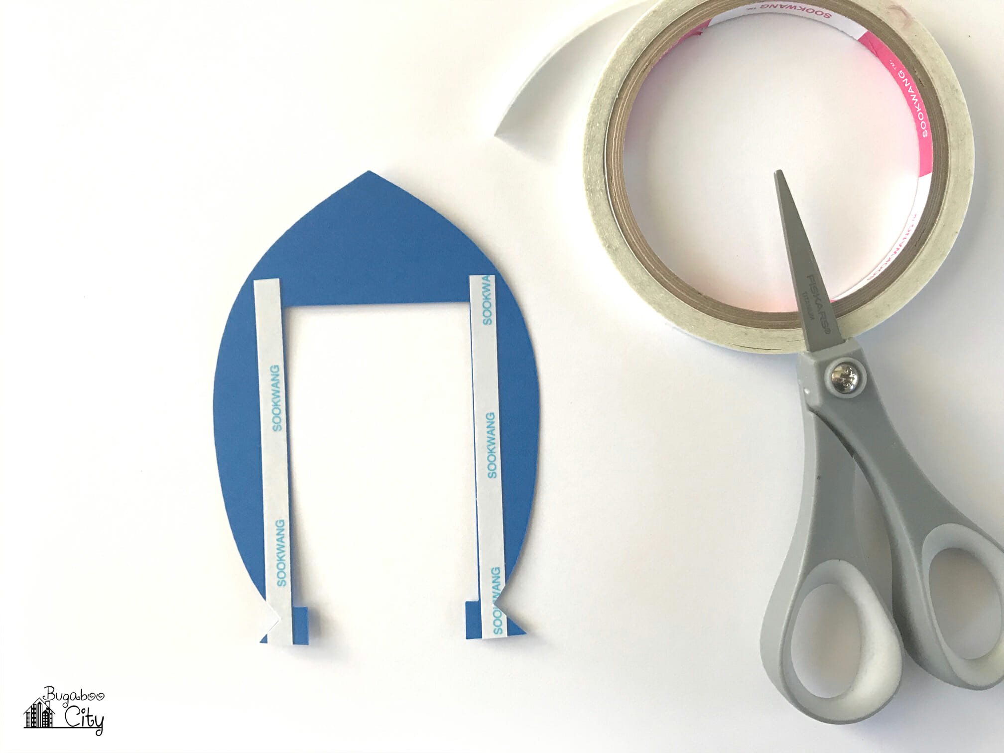Double-sided tape lines the rectangle cutout in the rocket ship piece of paper.
