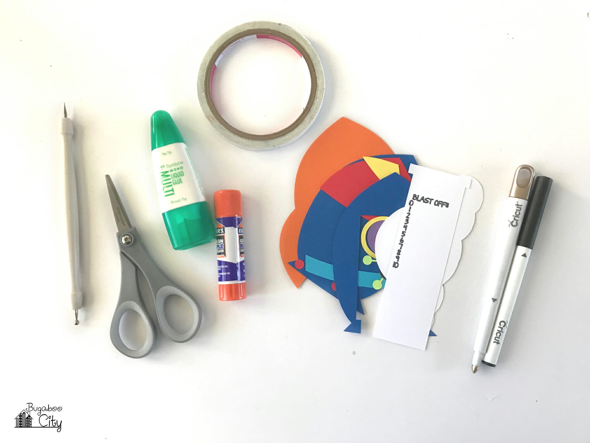 Supplies including scissors, double sided tape, Cricut pen, and cardstock pieces.